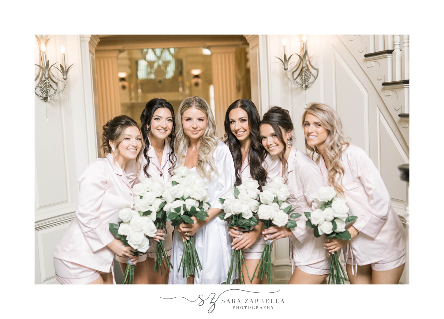 bride and bridesmaids in pink pajamas in lobby of Shepard's Run hold long stemmed white roses 