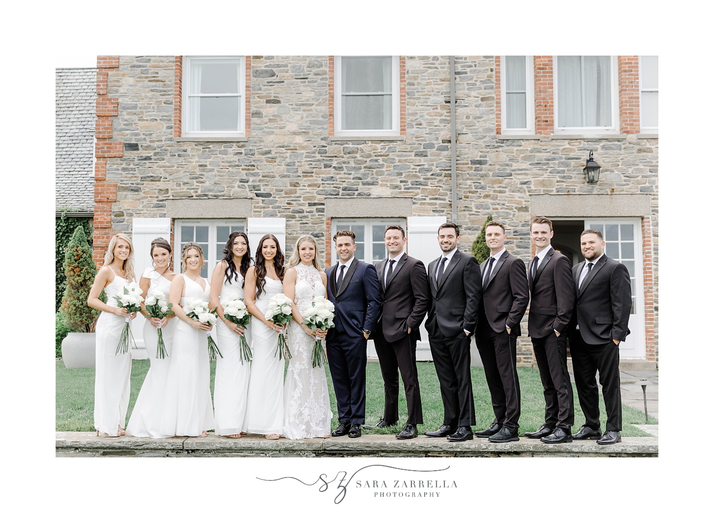 bride and groom stand with wedding party in garden outside stone building at Shepard's Run