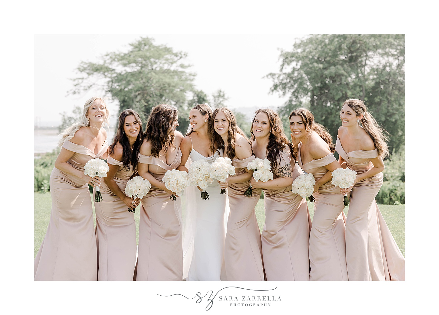bride smiles at bridesmaids in light pink gowns with white flowers 