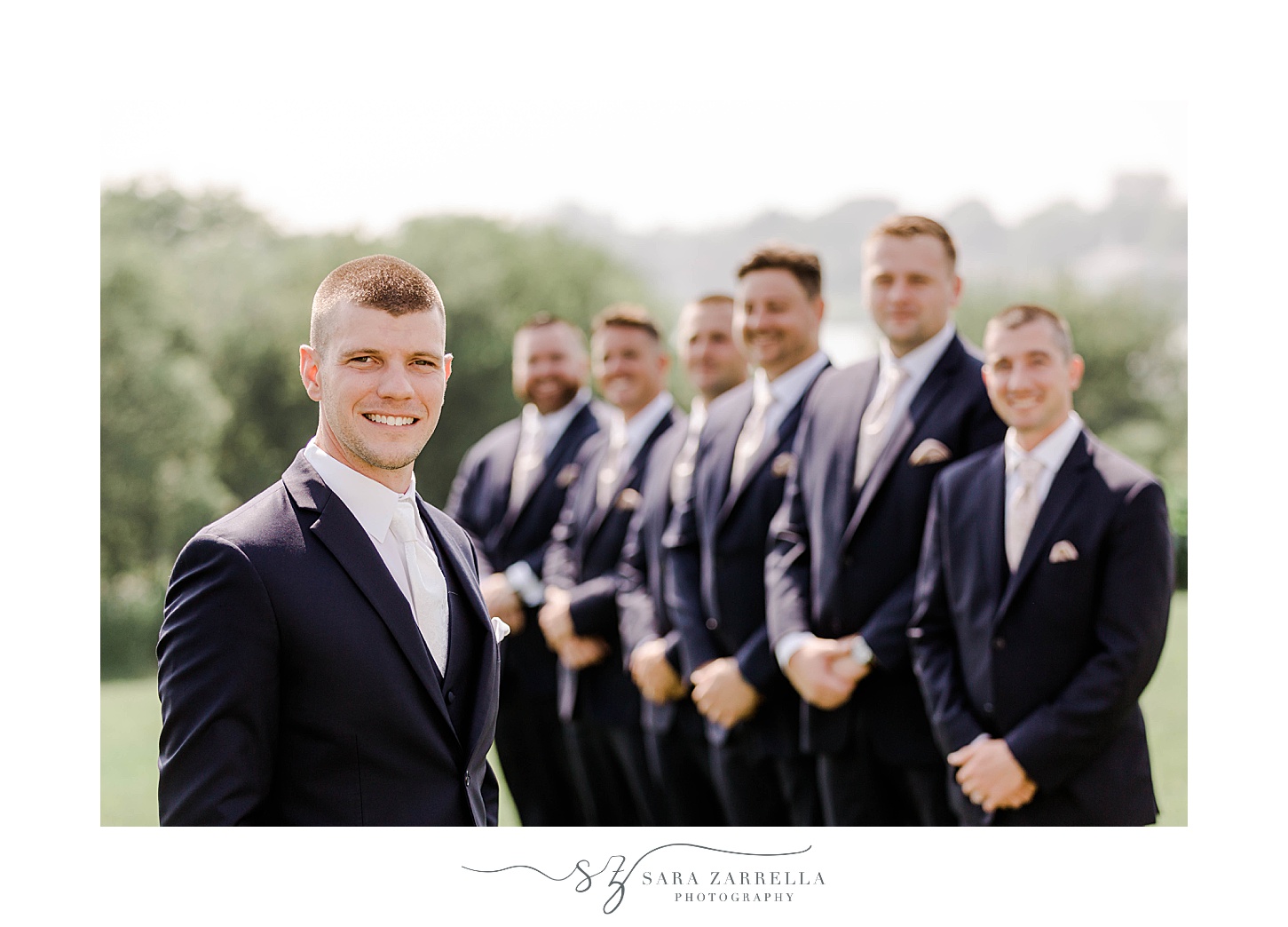 groom stands next to groomsmen in navy suits smiling 