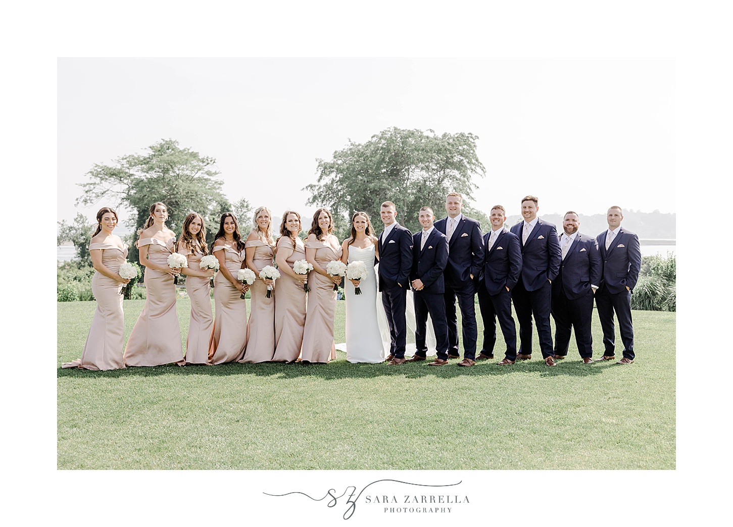 bride and groom stands with bridesmaids in pink gowns and groomsmen in navy suits 