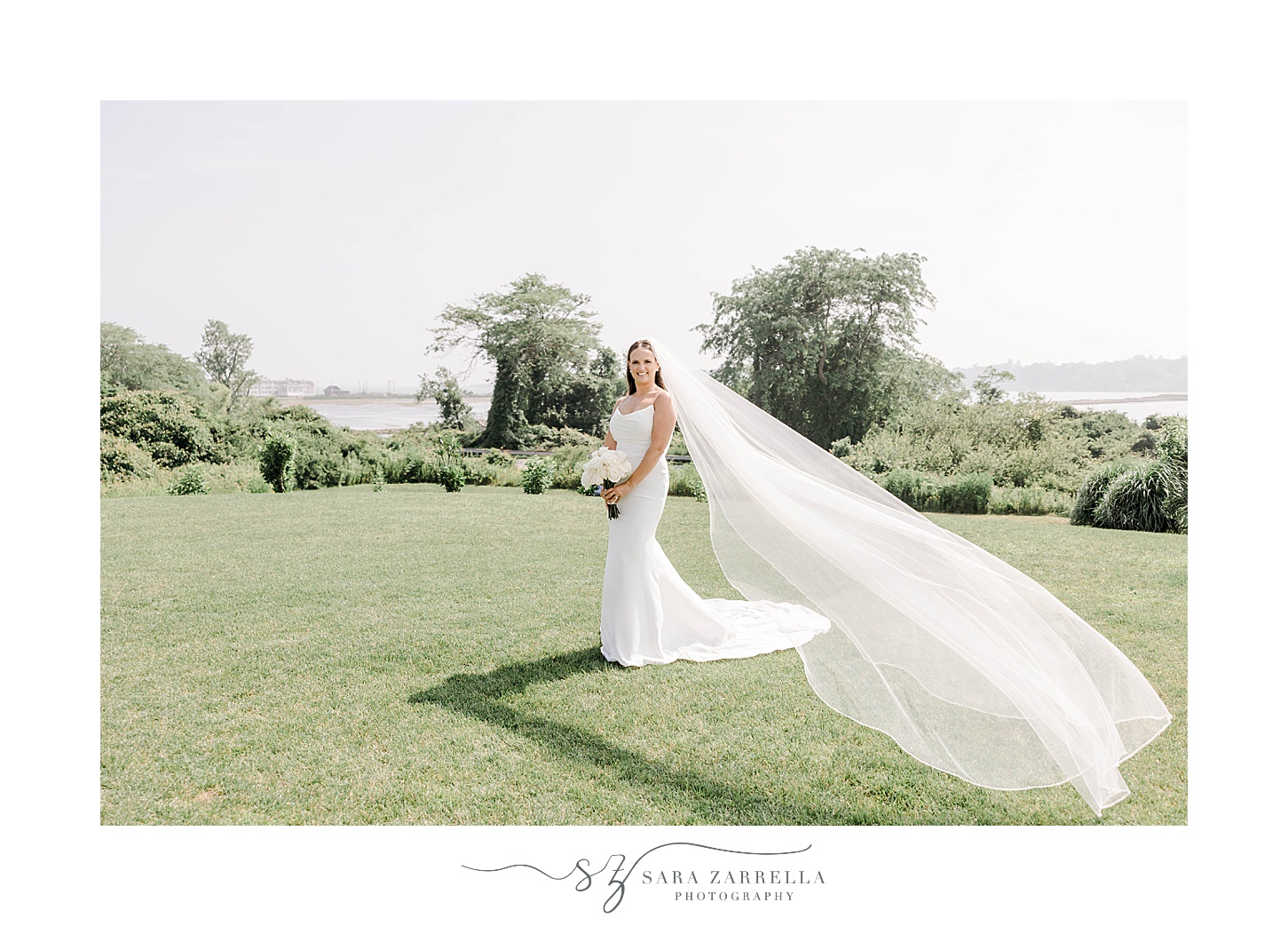 bride stands on lawn holding bouquet with veil around her 