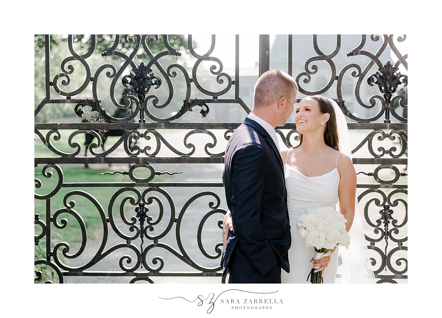 bride leans up to kiss groom in front of wrought iron gate 