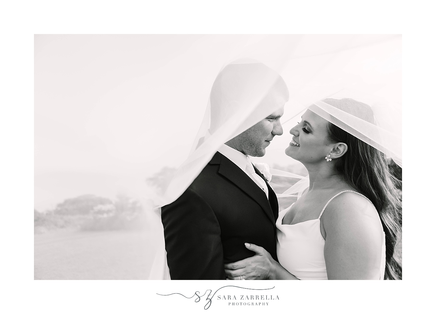 black and white photo of couple hugging under bride's veil 