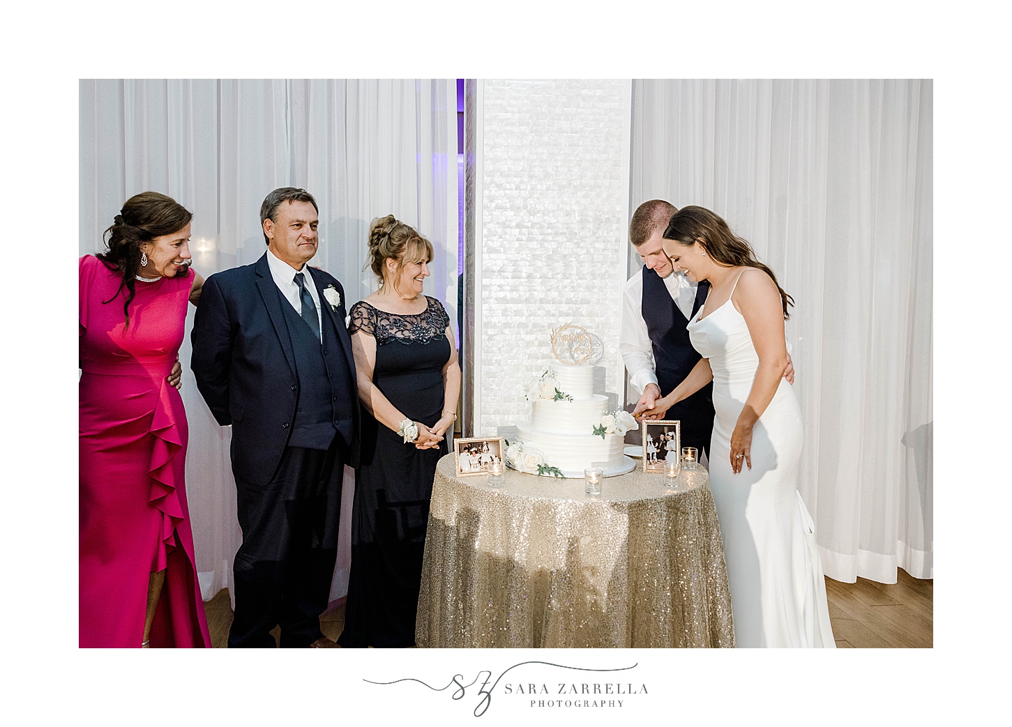 bride and groom cut wedding cake with parents around them 