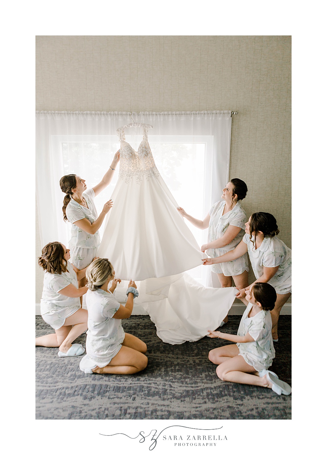 bride and bridesmaids look at wedding gown hanging in window at Newport Harbor Island Resort