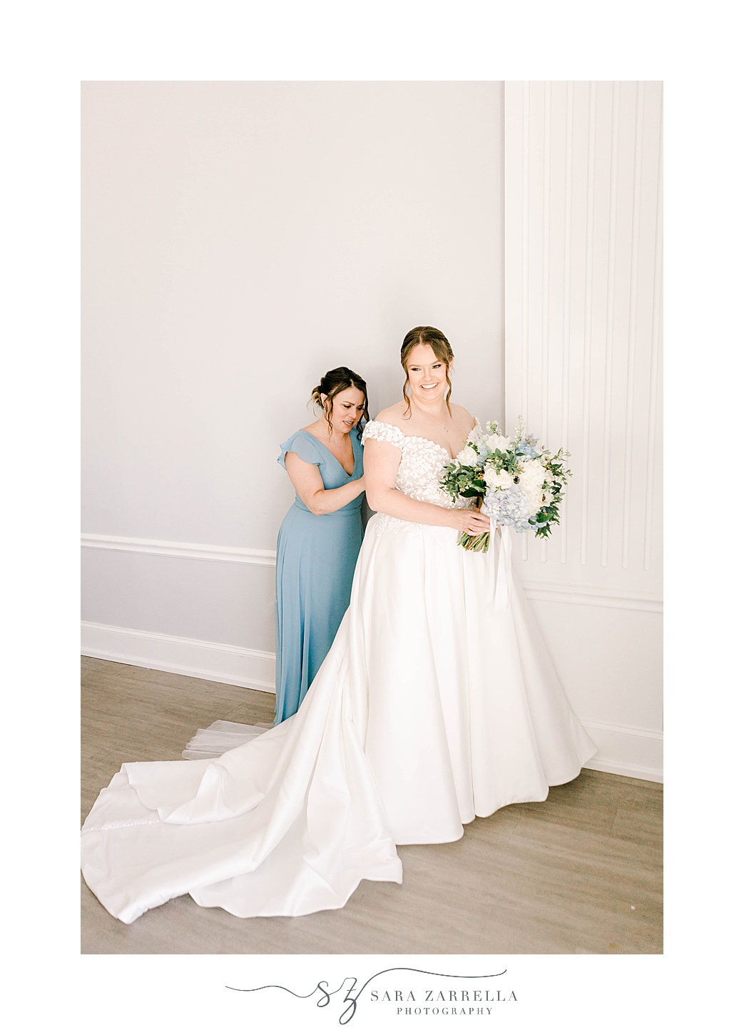 bridesmaid in light blue gown helps bride into wedding dress
