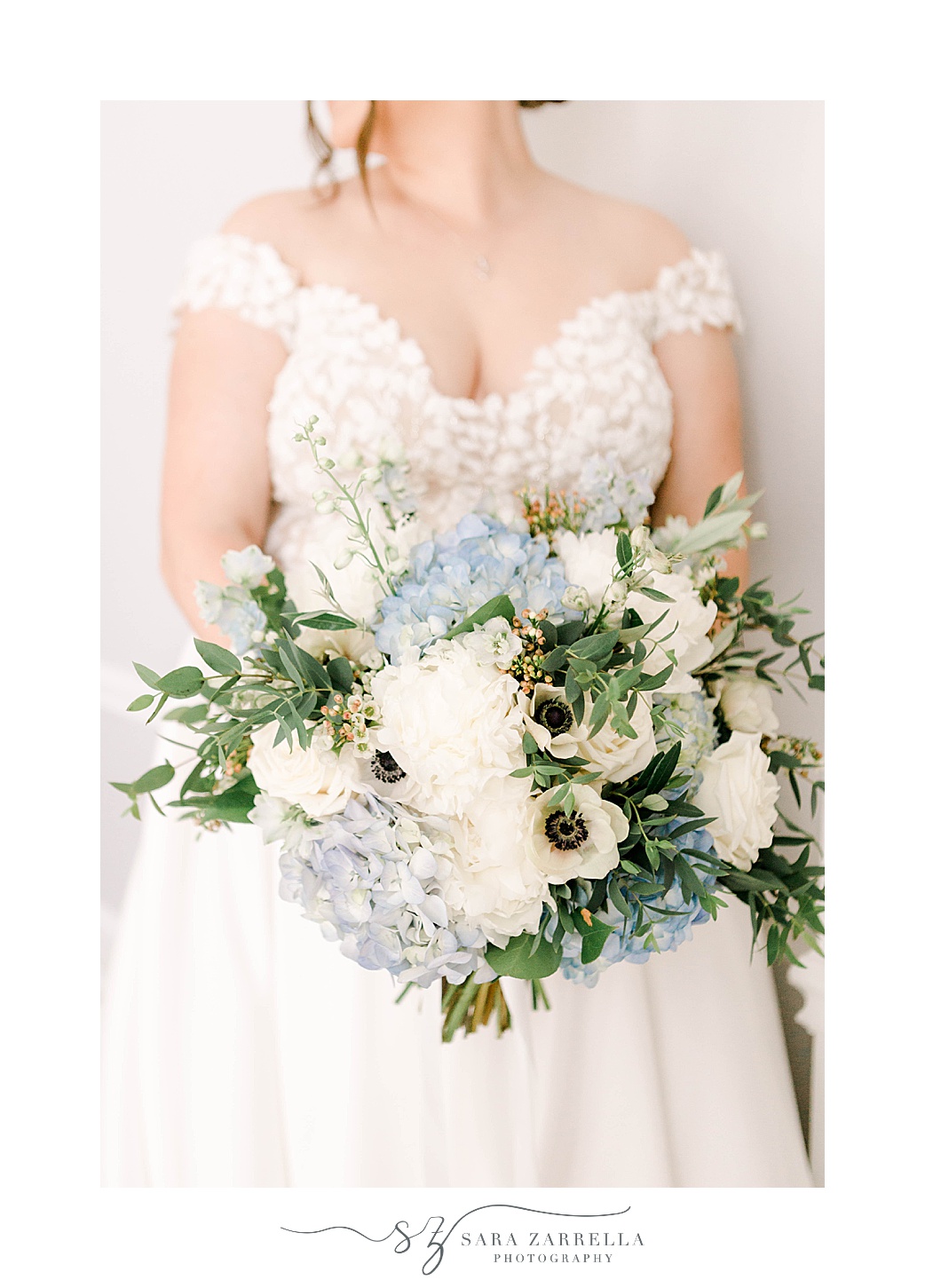 bride holds bouquet of blue and white flowers in off-the-shoulder lace wedding gown