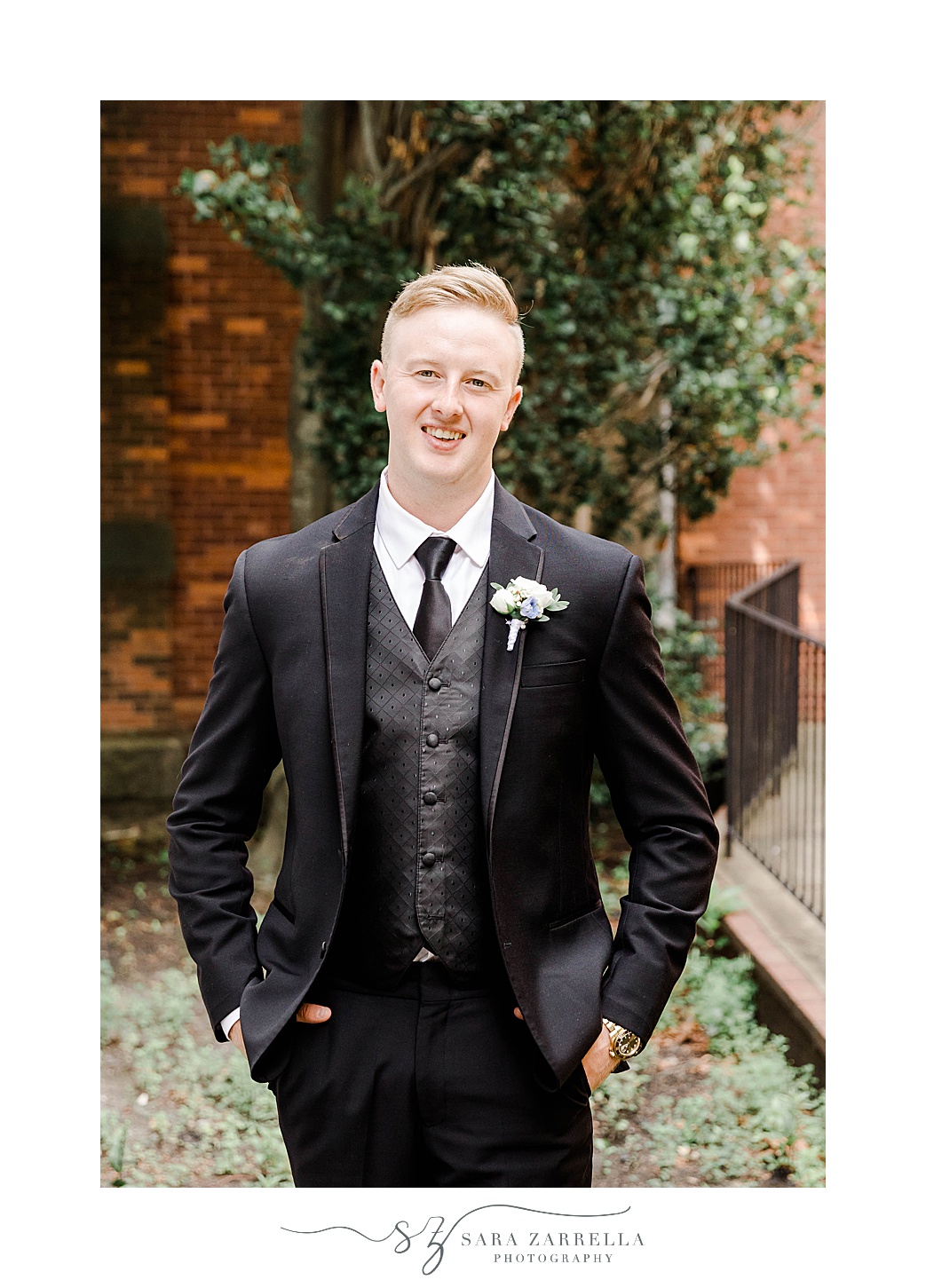 groom poses in black suit with white boutonnière for summer wedding