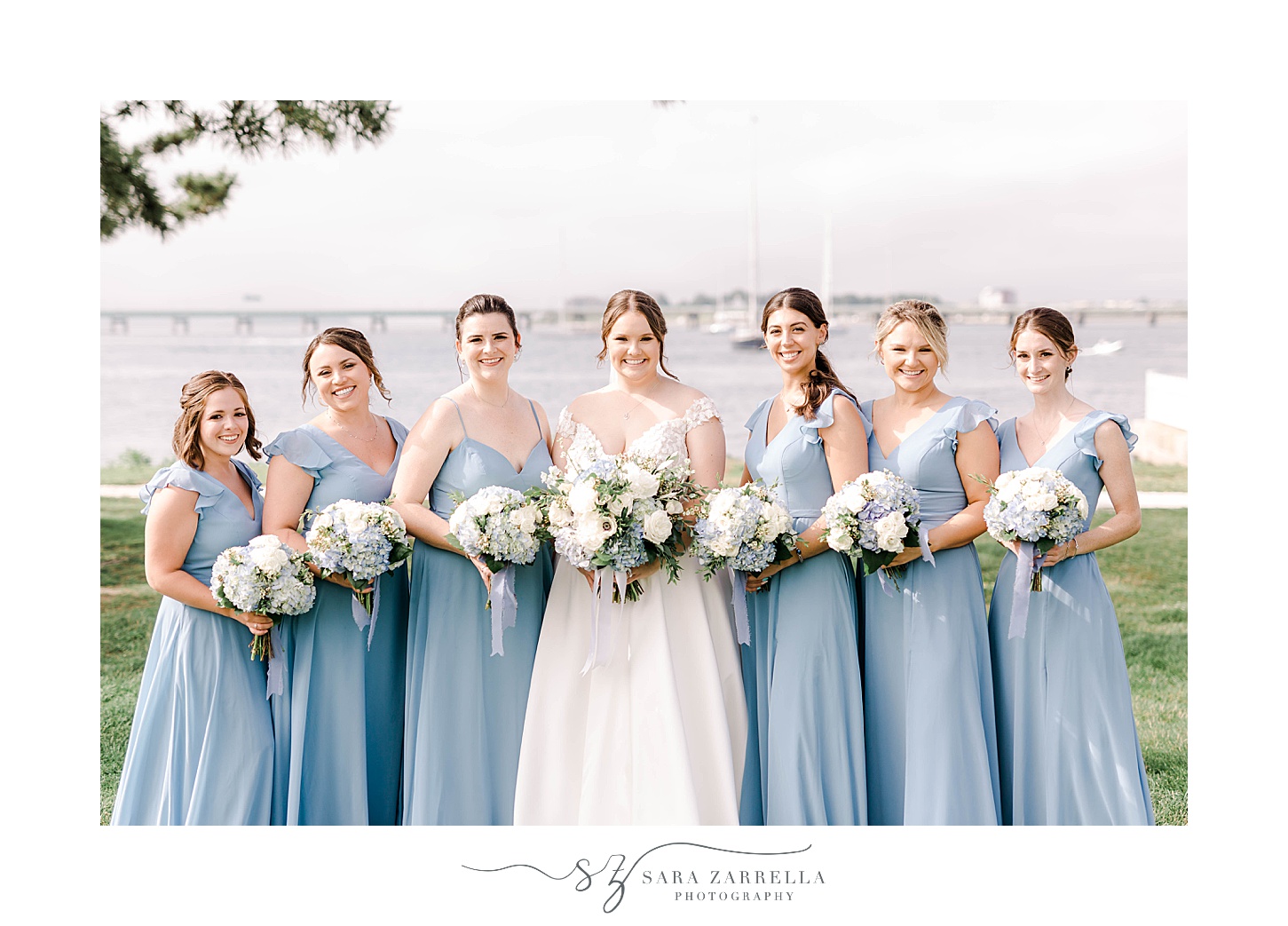 bride poses with bridesmaids in light blue gowns with white and blue flowers at Newport Harbor Island Resort