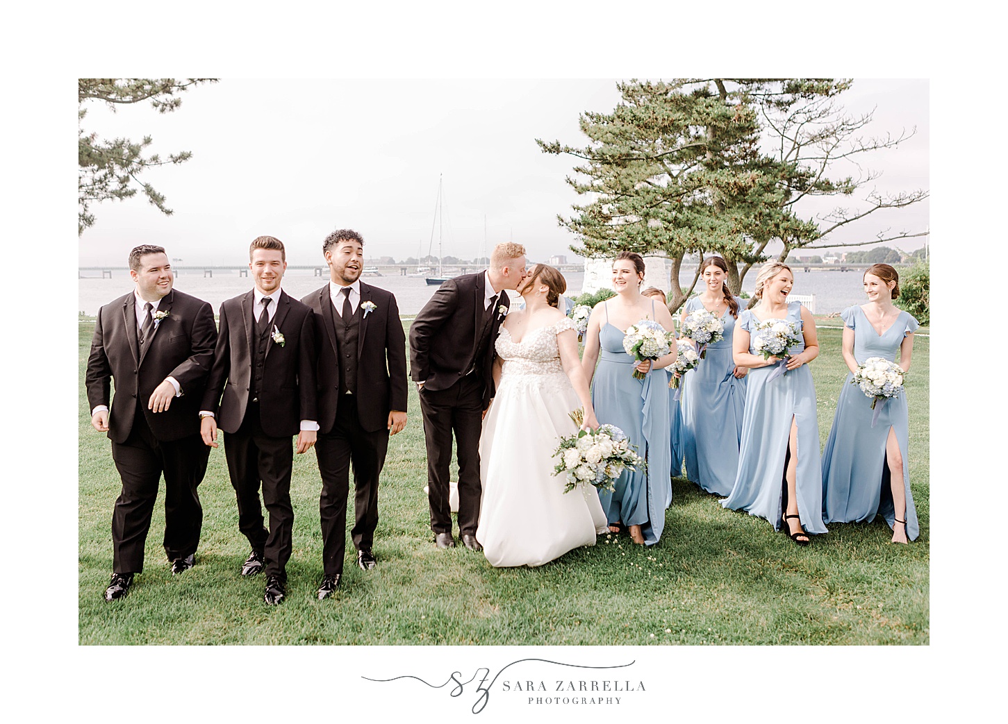 bride and groom walk with wedding party in front of Newport Lighthouse 