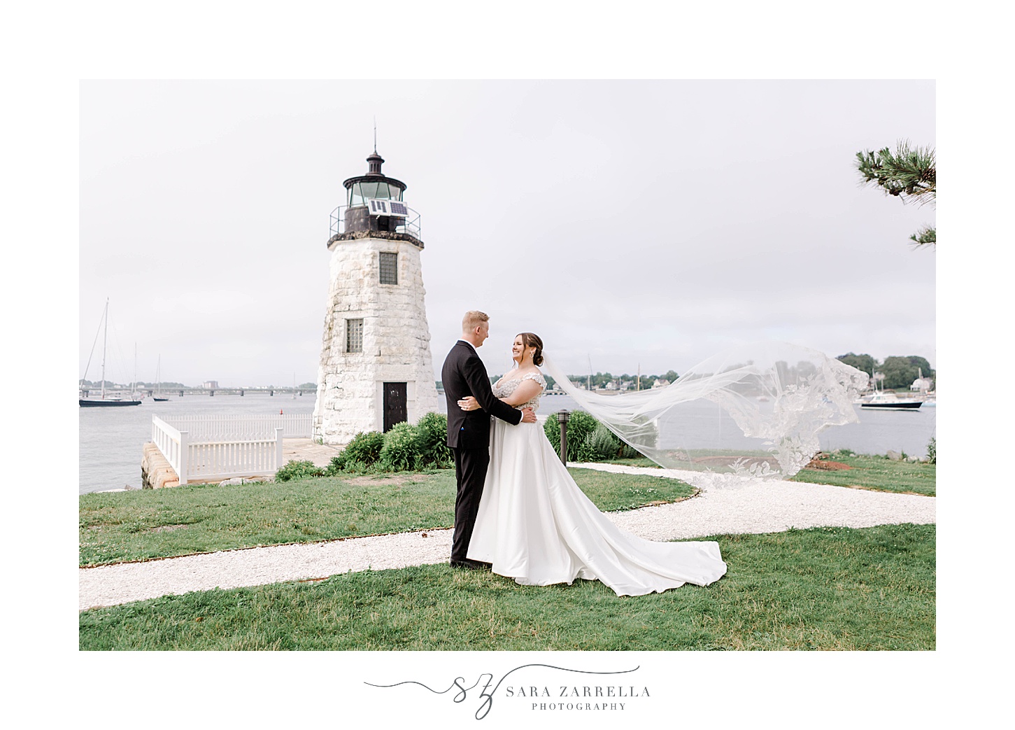 bride and groom hug in front of Newport Lighthouse with bride's veil floating behind them
