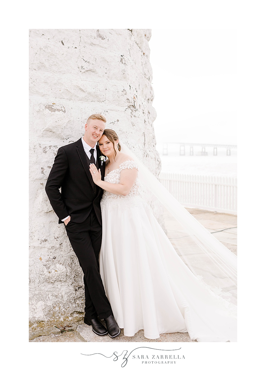 bride leans into groom's chest in front of Newport Lighthouse 