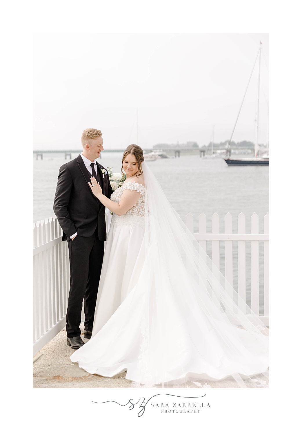 groom hugs bride along gate at Narragansett Bay