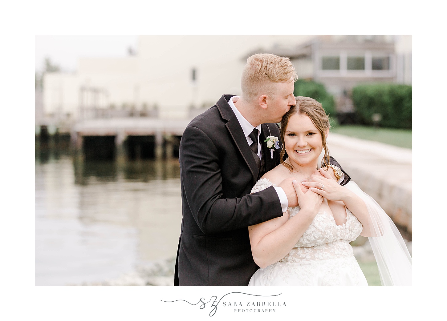 groom hugs bride from behind kissing her forehead at Narragansett Bay