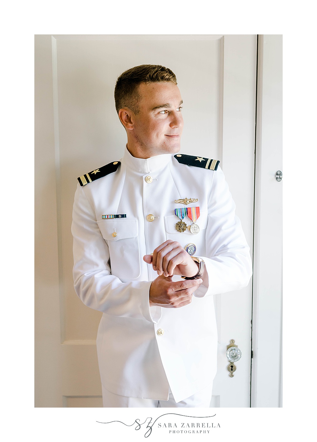 groom stands in Naval officer's white uniform in Rhode Island
