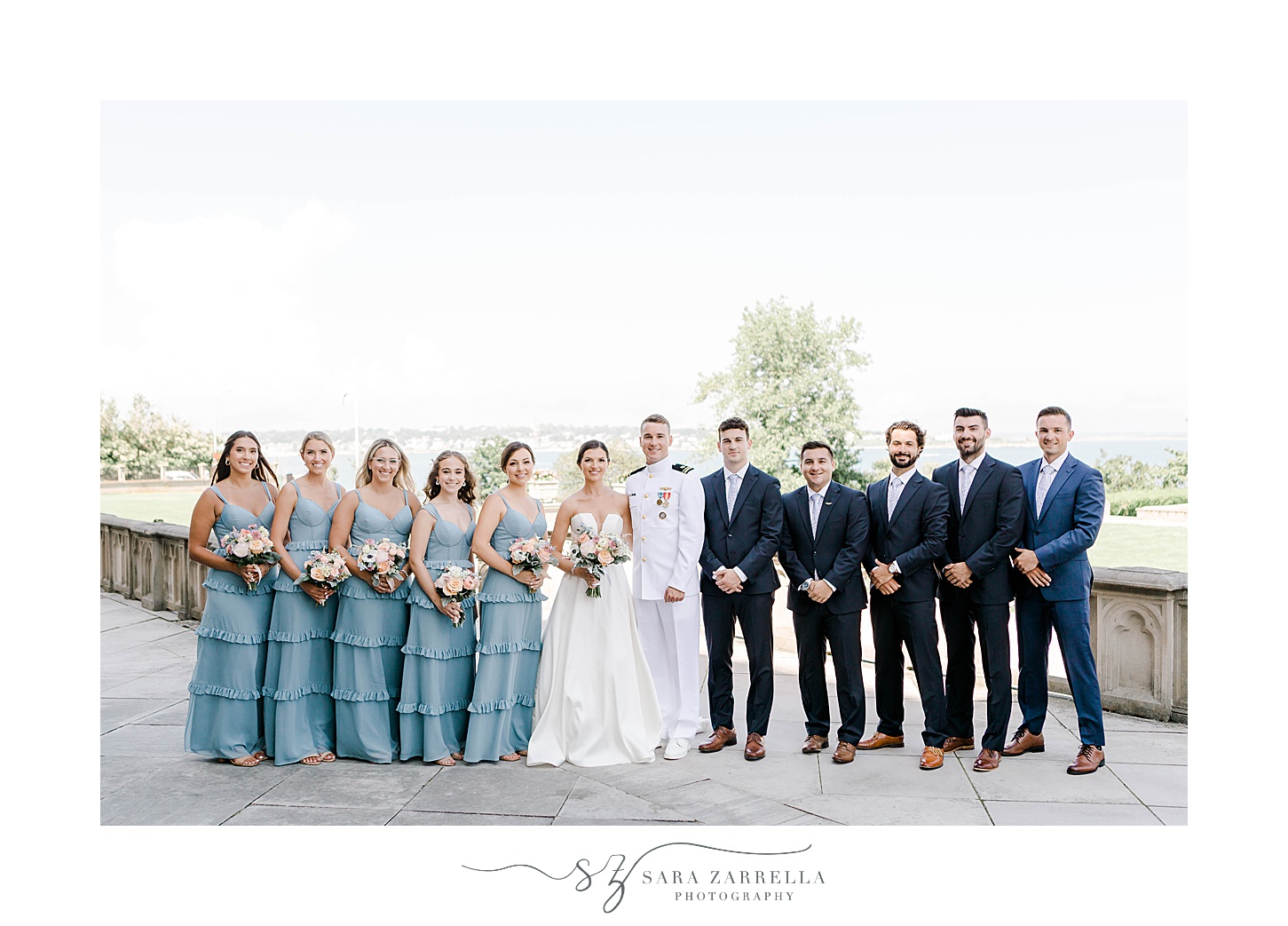 bride and groom stand with wedding party in blue dresses and suits