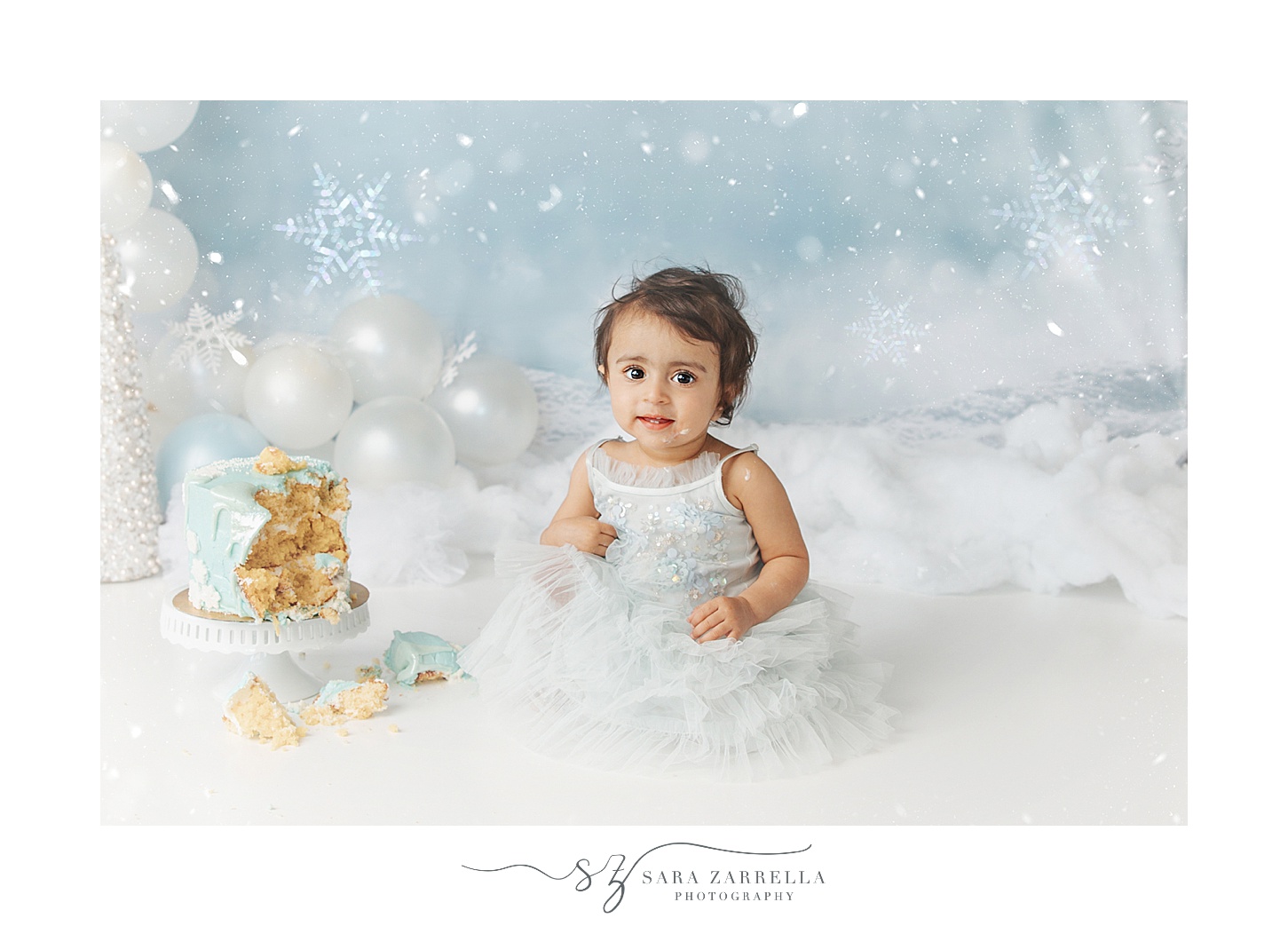 one year old girl sits in blue winter wonderland themed cake smash with Sara Zarrella Photography