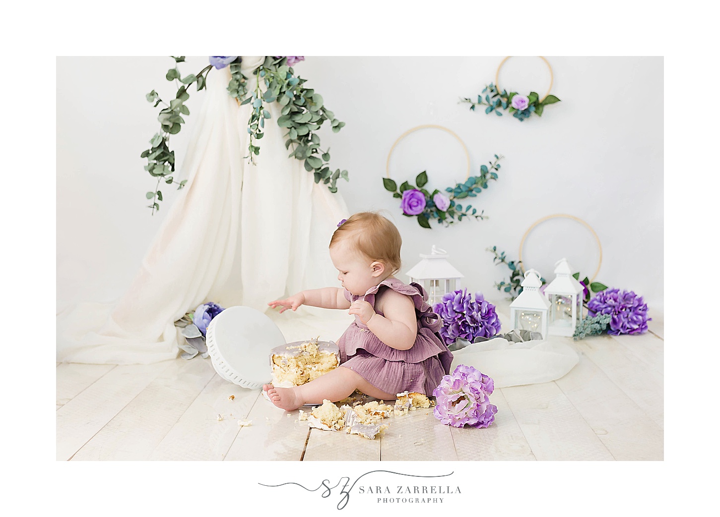 toddler in purple dress eats cake off floor during cake smash portraits with Sara Zarrella Photography