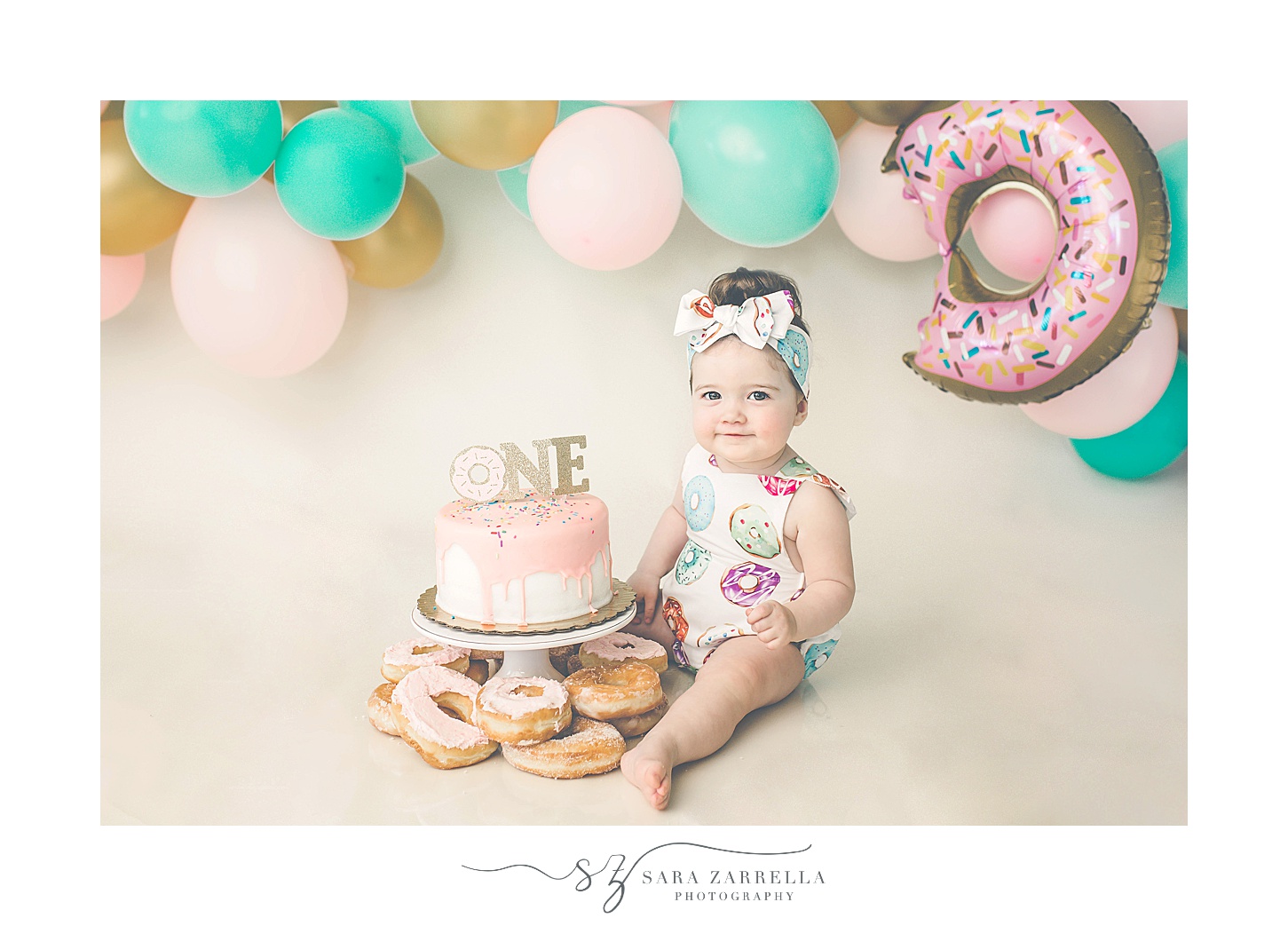 girl sits by cake on tier with donuts around it for cake smash portraits with Sara Zarrella Photography