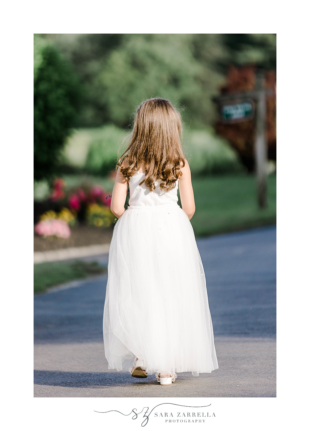 flower girl in white dress walks away from ceremony in gardens at Kirkbrae Country Club