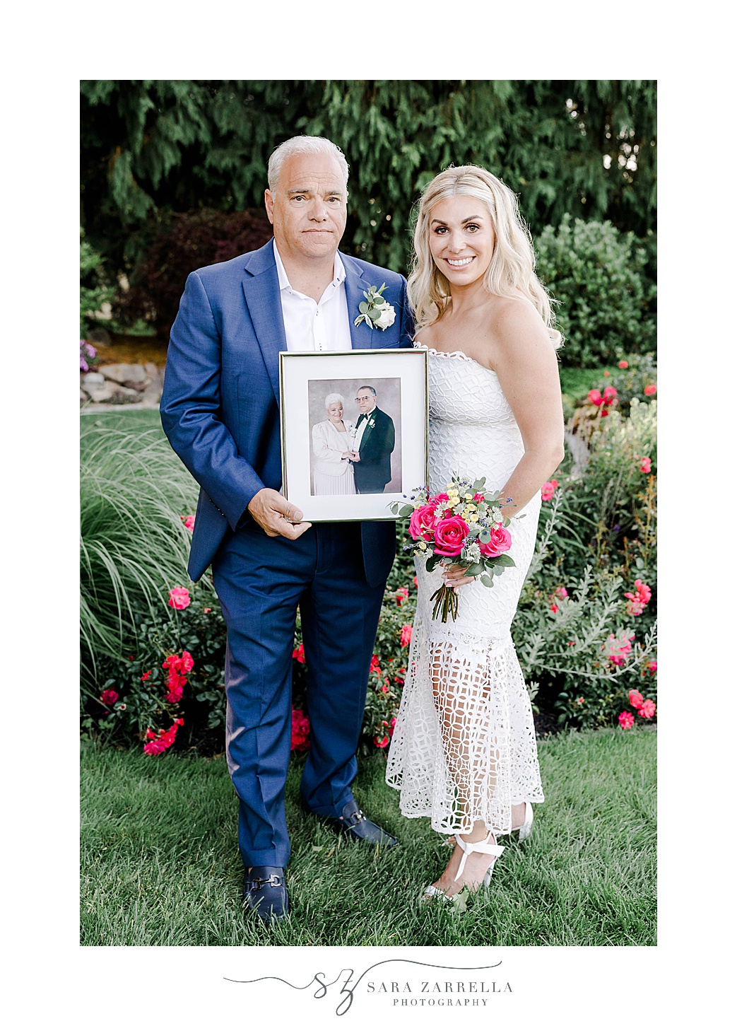 bride and groom stand holding photo of parents on wedding day