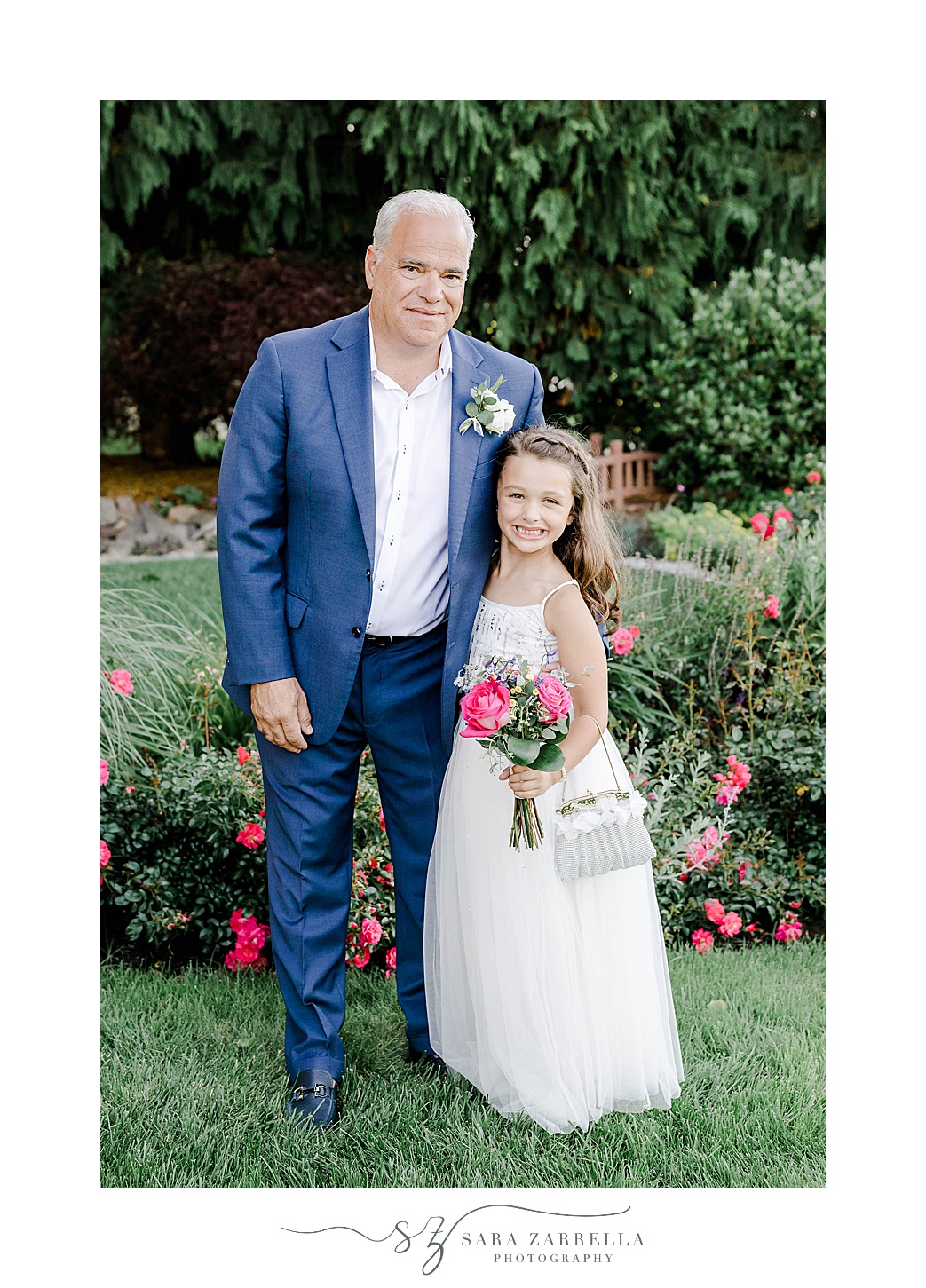 groom in blue suit hugs flower girl in white dress