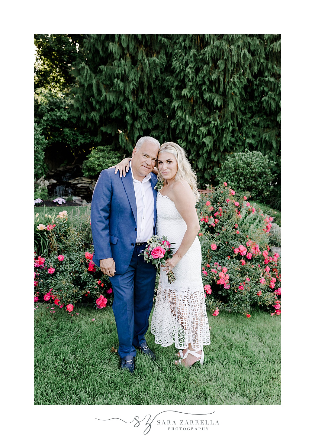 bride holding bright pink flowers hug groom in blue suit in gardens of Kirkbrae Country Club