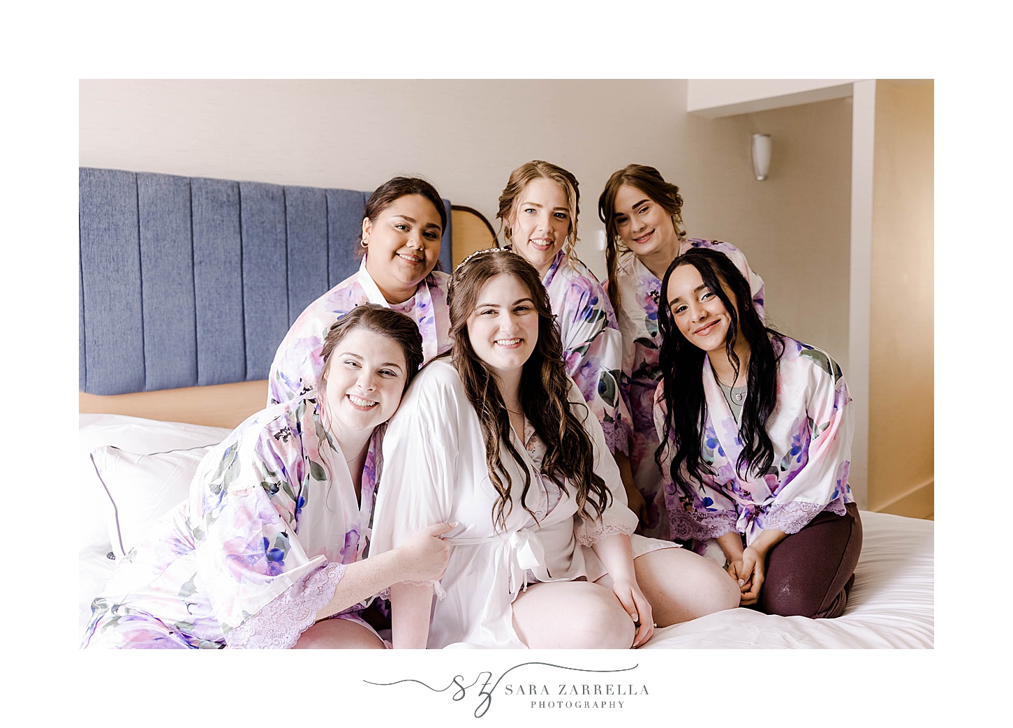 bride sits on bed with bridesmaids in matching floral robes 