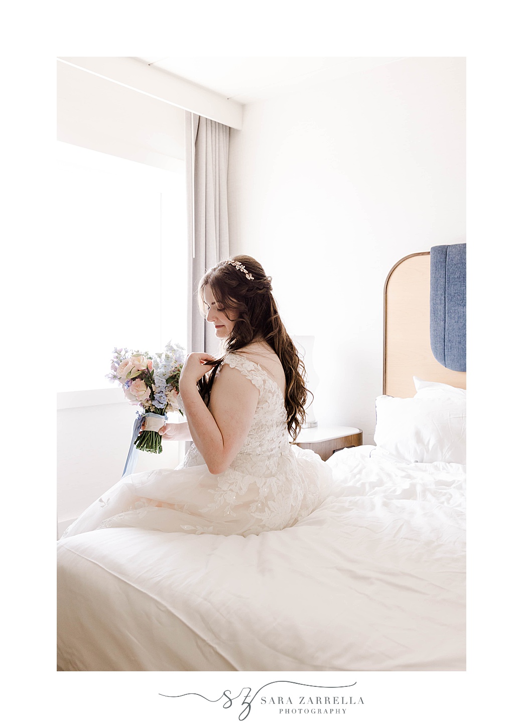 bride sits on bed in wedding dress holding pastel bouquet 