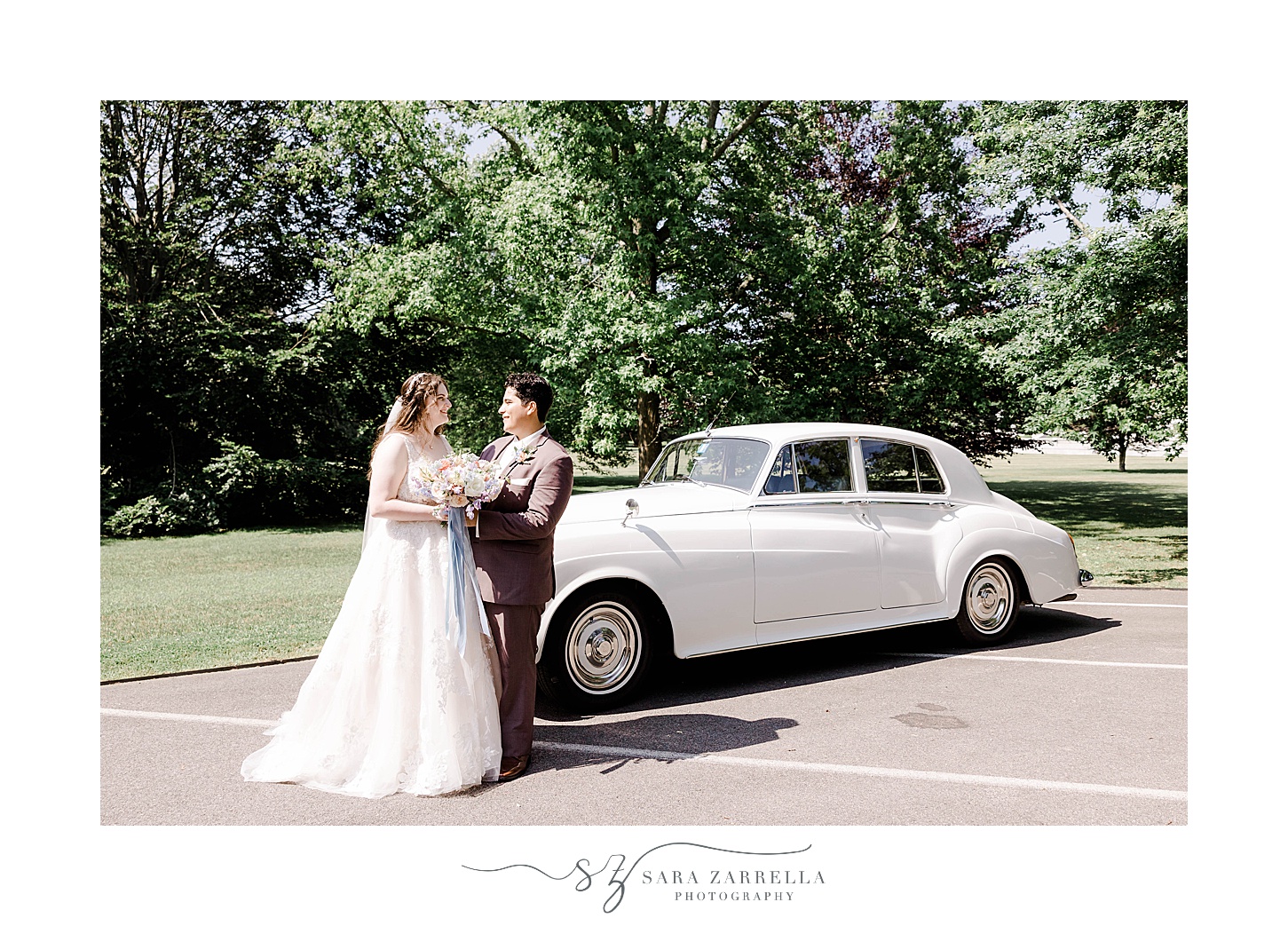 bride and groom hug leaning against the front of white classic car in Rhode Island