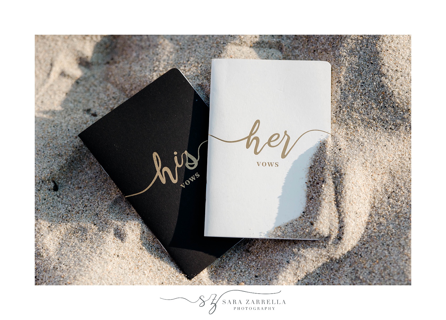 black, white, and gold vow booklets on sand of v