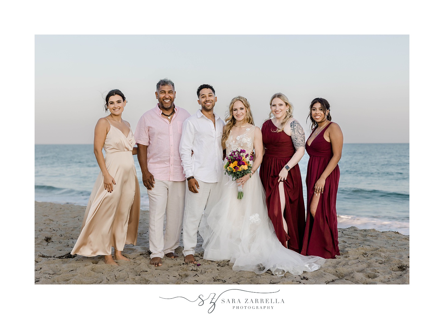 bride and groom pose with bridal party in red dresses on Charlestown Beach
