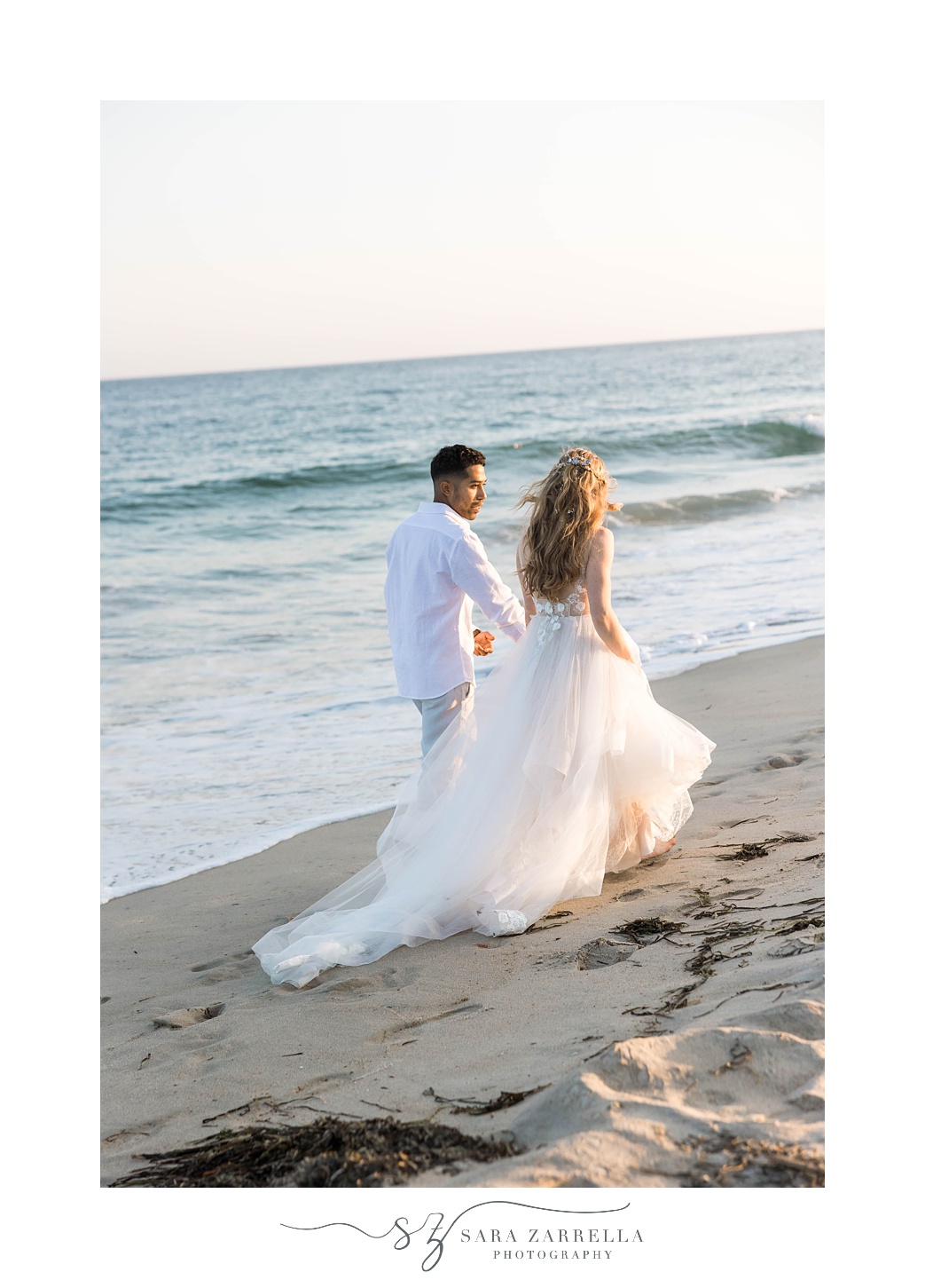 newlyweds hold hands walking on sand in front of ocean at Charlestown Beach