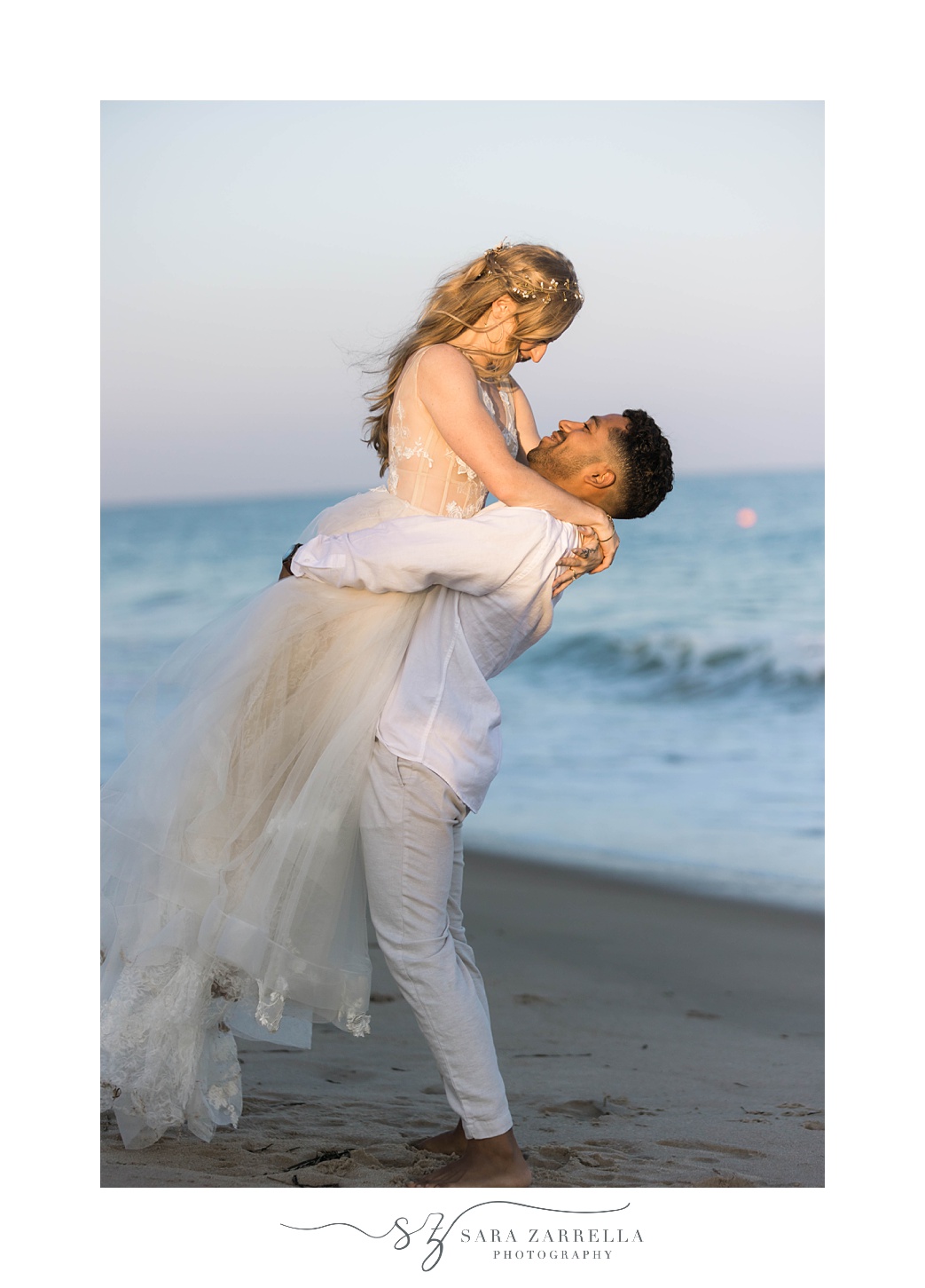 groom lifts up bride smiling at her on RI beach 