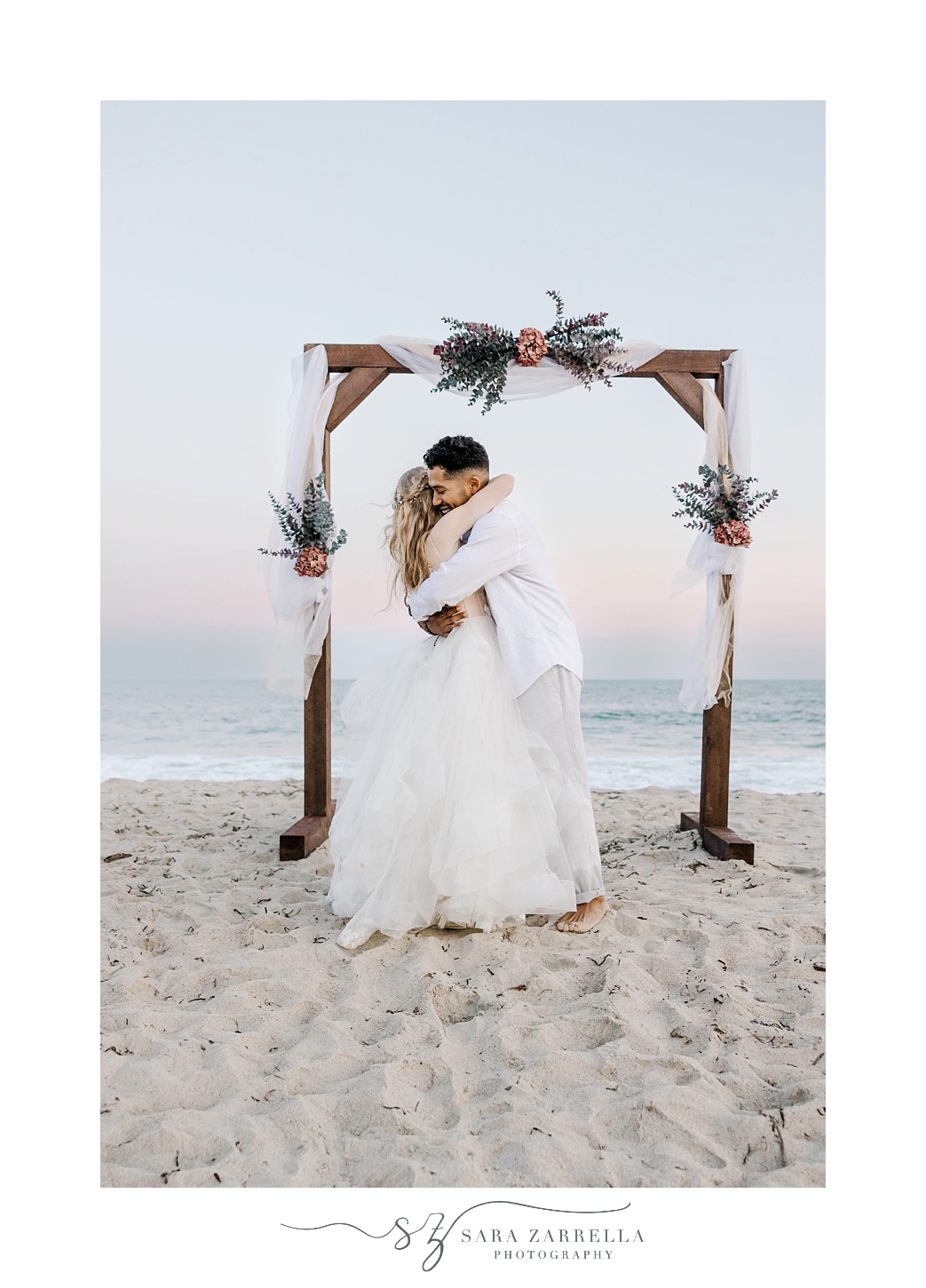 bride and groom kiss under wooden arbor with white fabric