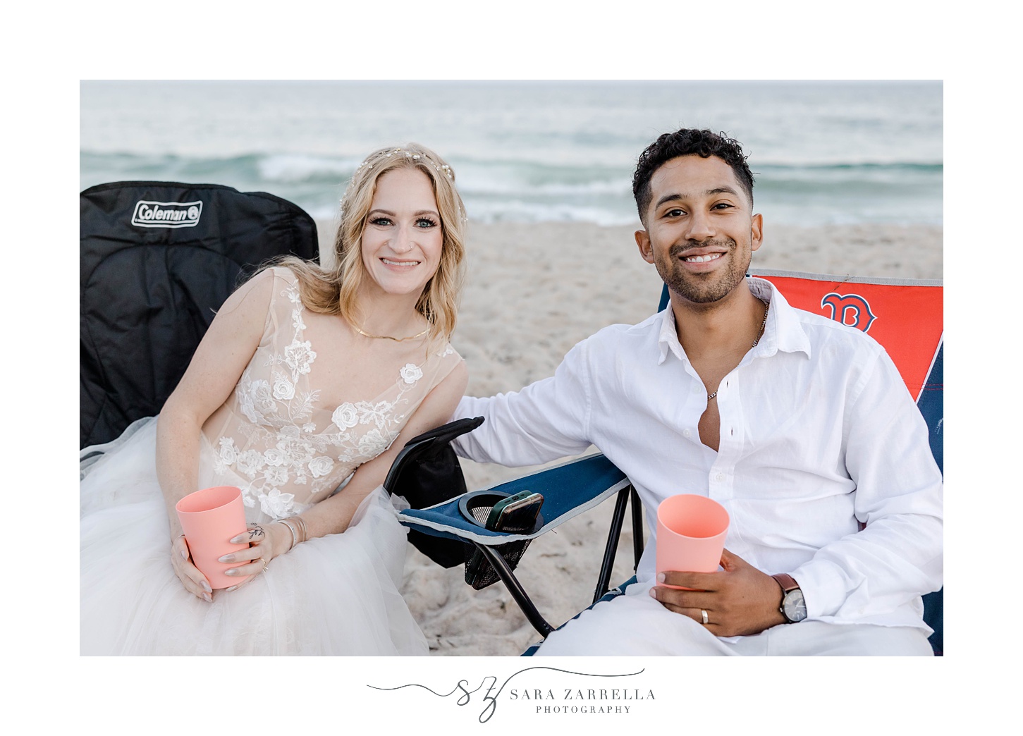 bride and groom sit holding custom plastic cups during beach wedding reception in Rhode Island