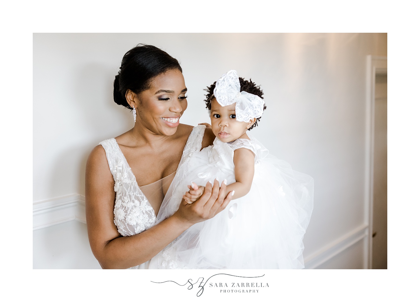 bride holds daughter in white dress with big bow before RI wedding day
