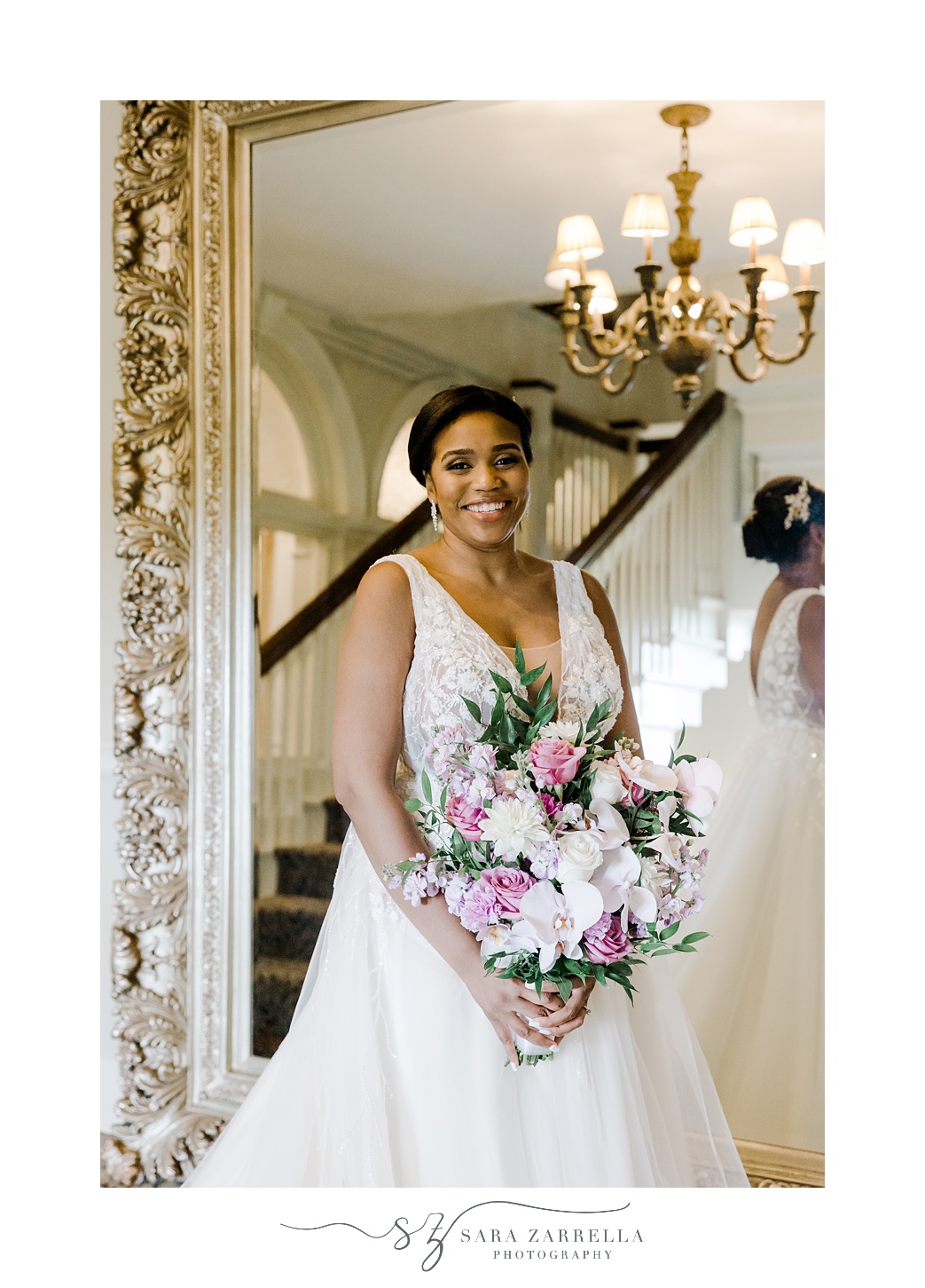 bride holds bouquet of white and purple flowers in front of gold framed mirror at OceanCliff Hotel