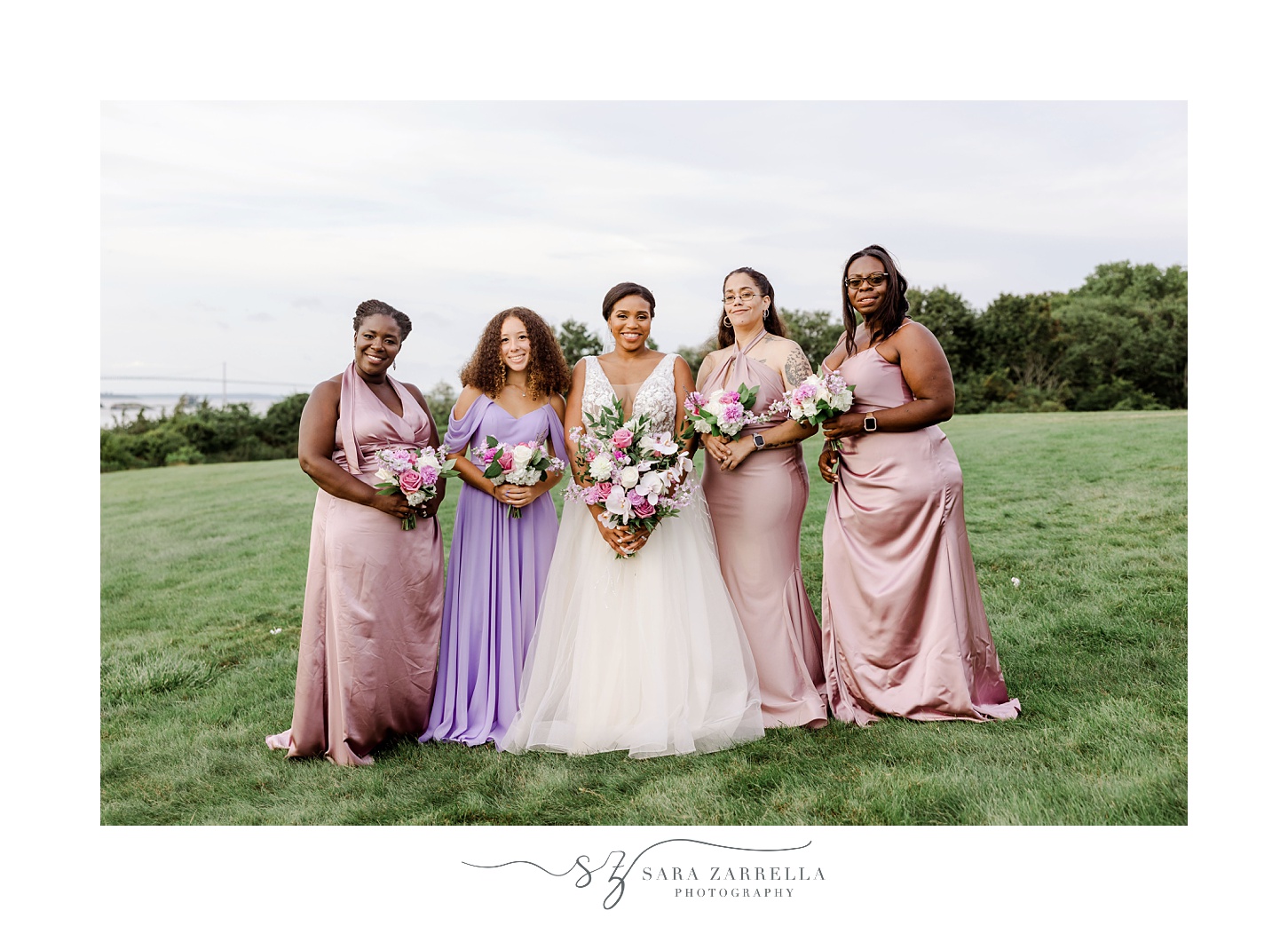 bride stands with bridesmaids in pink and purple gowns