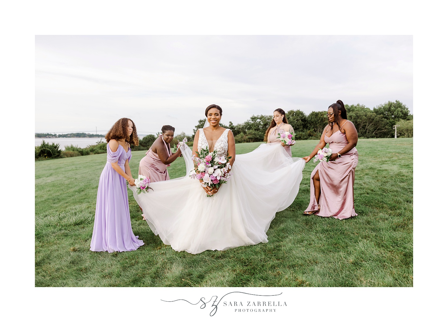 bridesmaids in purple and pink dresses help bride with wedding dress skirt