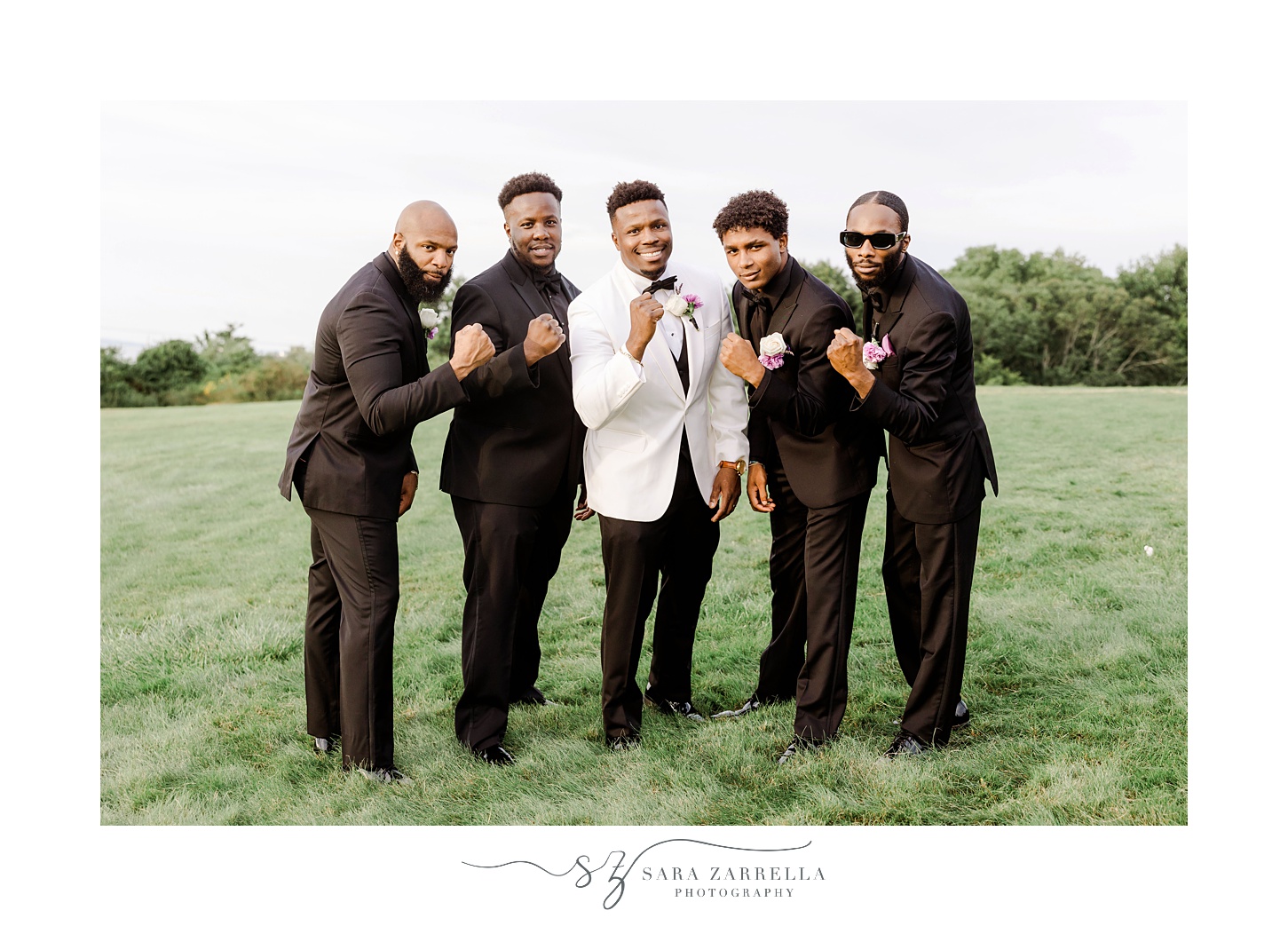 groom and groomsmen stand together making fists on hill at OceanCliff Hotel