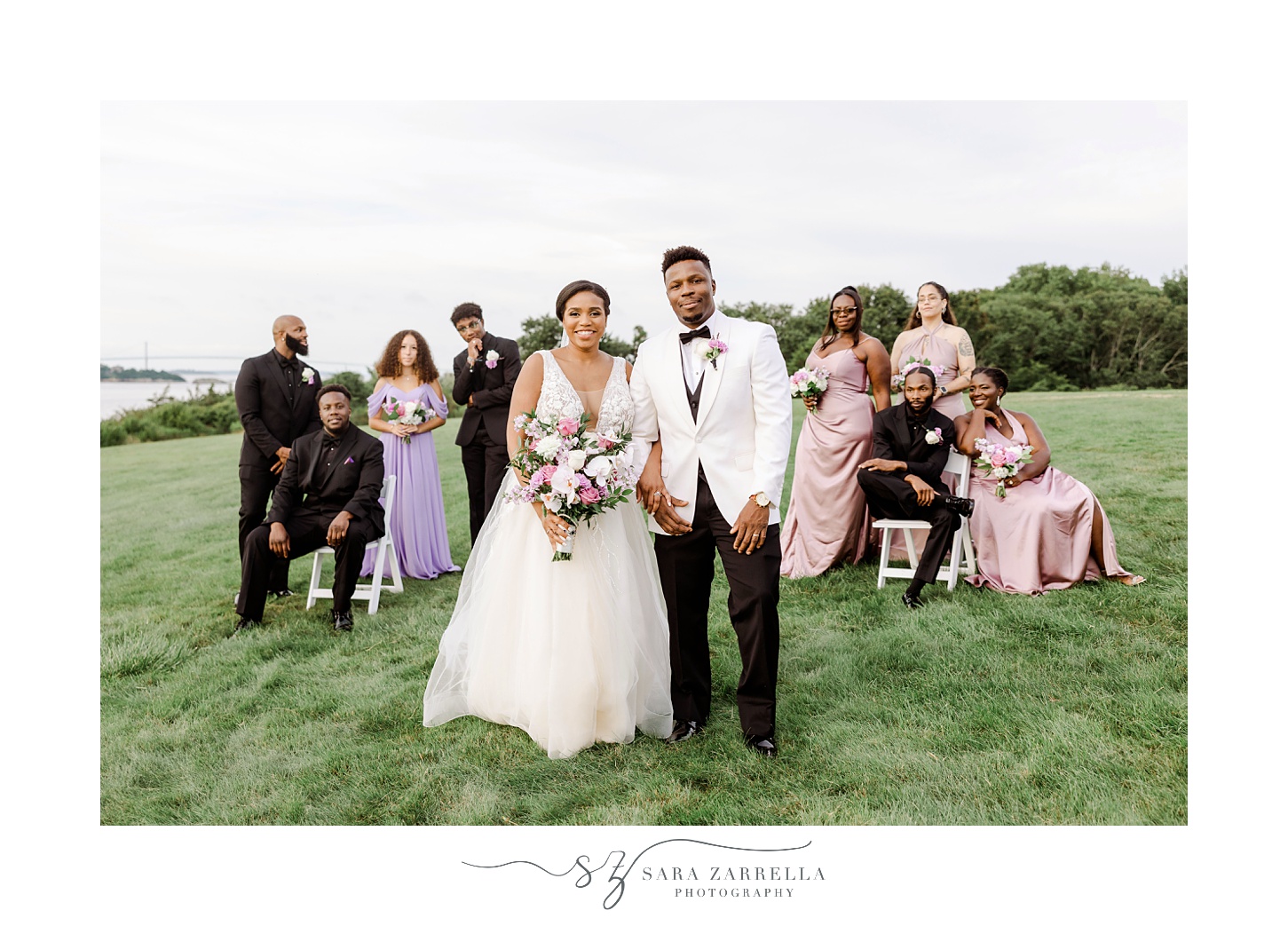 newlyweds stand in front of wedding party in pink and purple gowns and black suits 