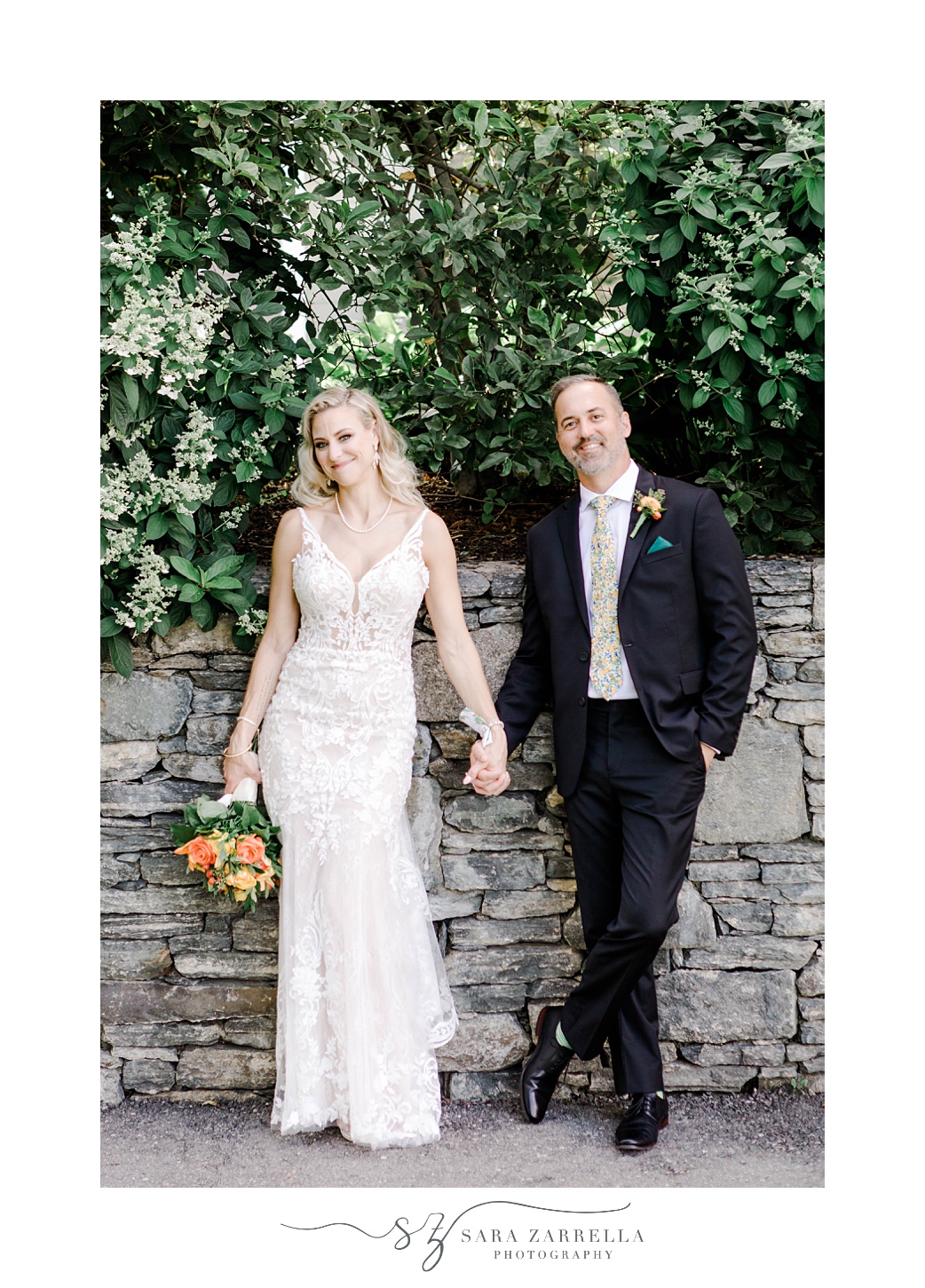groom and bride lean against stone wall holding hands at Pleasant Valley Country Club