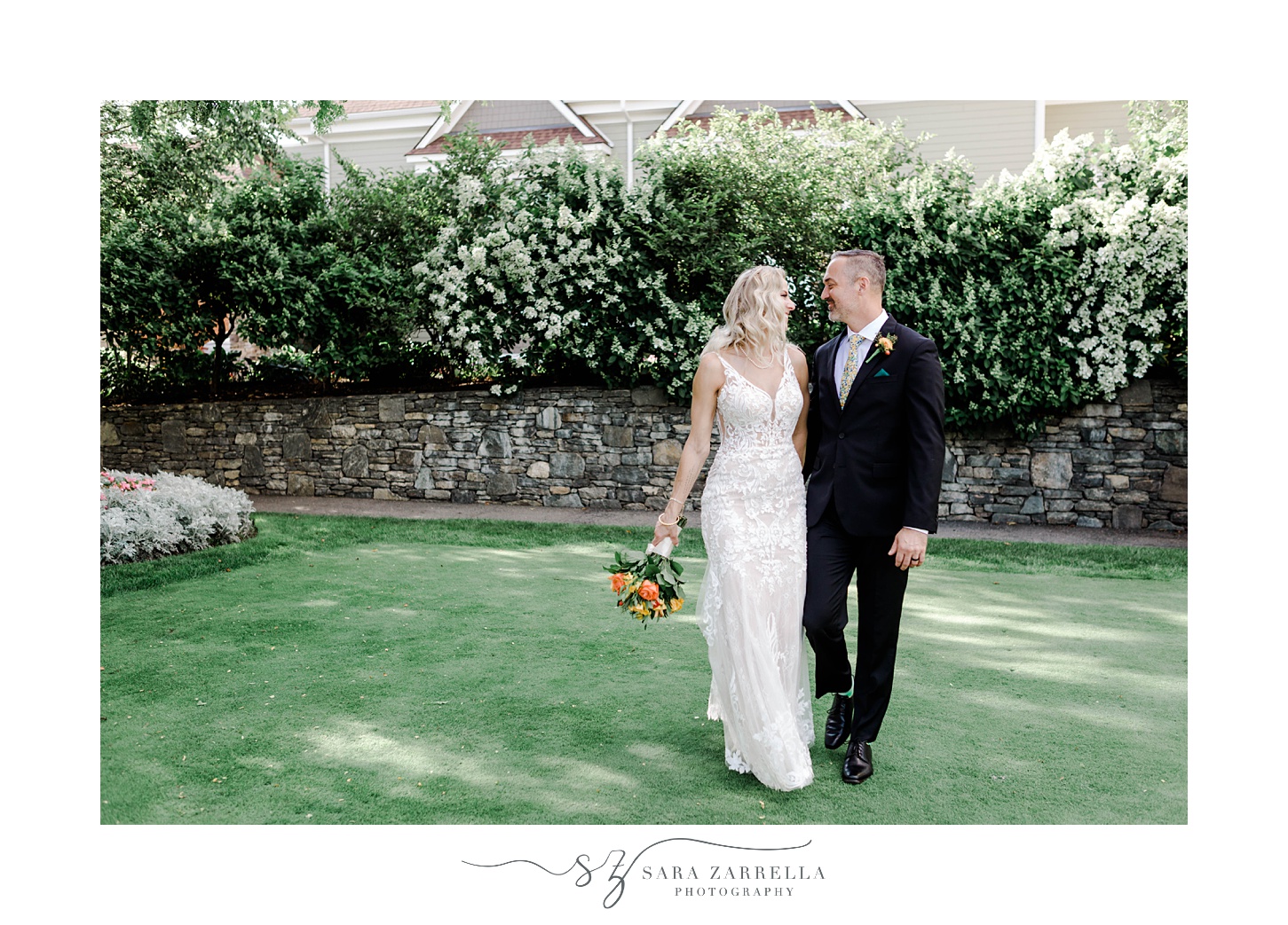 bride and groom hold hands walking on lawn while bride holds bright bouquet next to her hip
