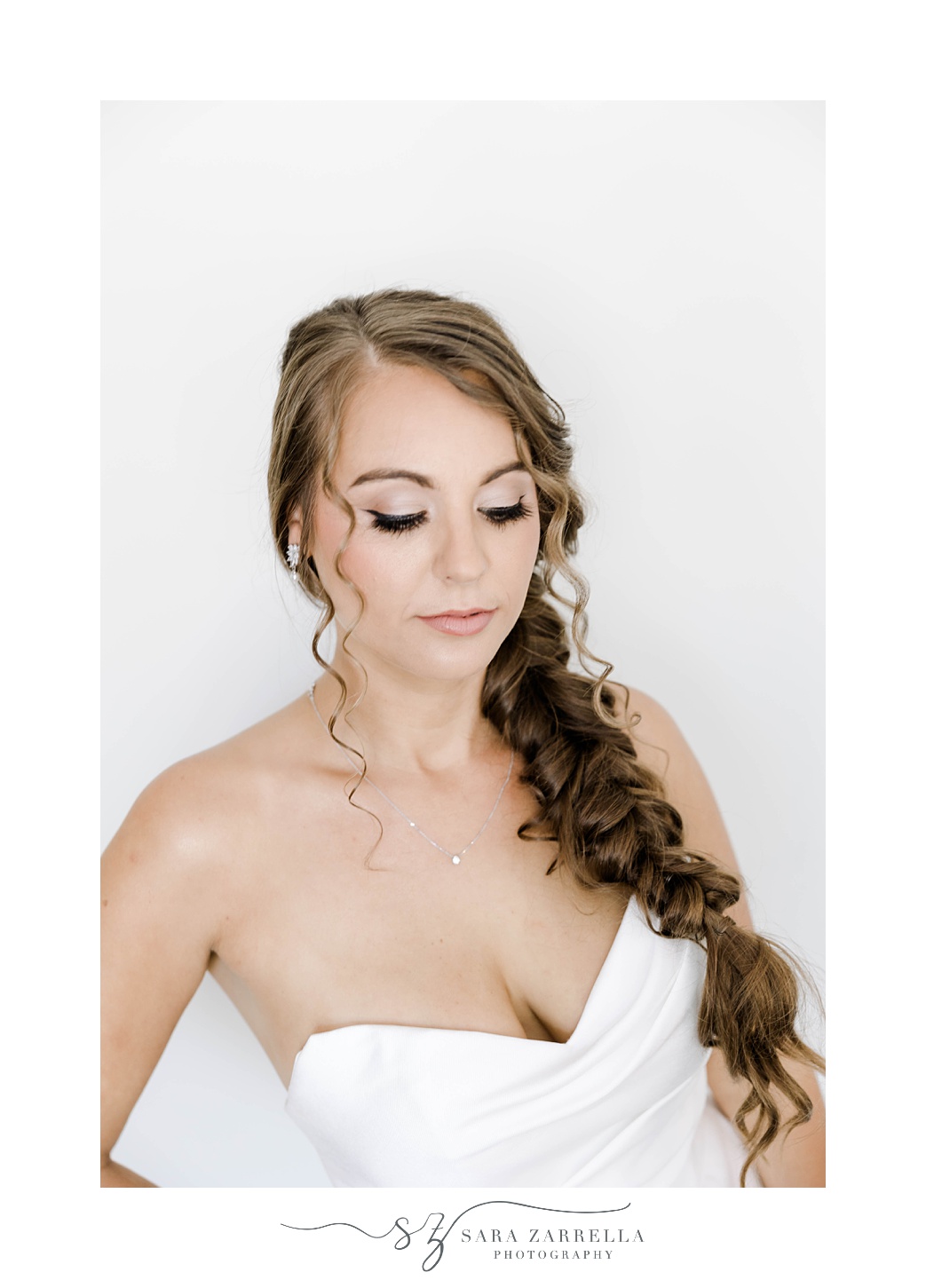 bride looks down at strapless wedding gown with fishtail braid on shoulder 