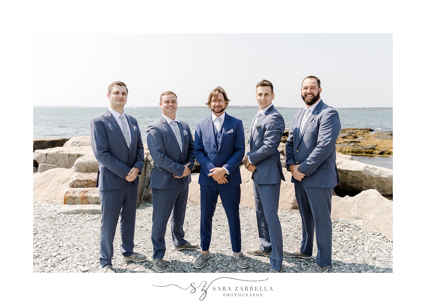 groom poses with groomsmen in blue suits with hands in front of them 