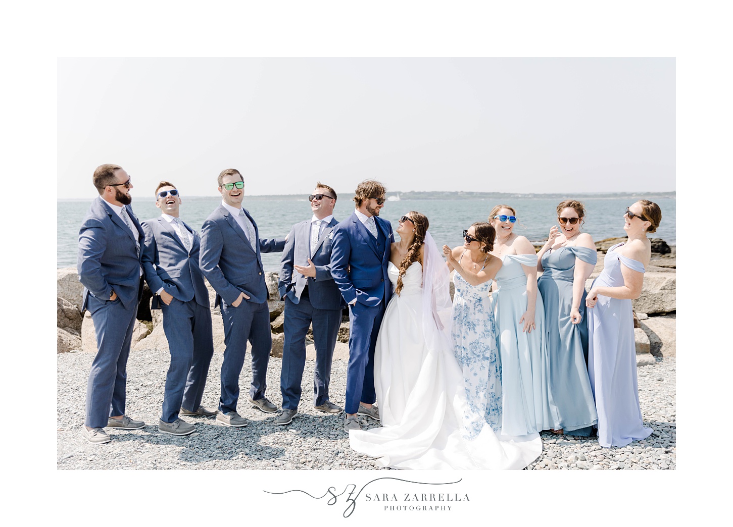 bride and groom hug with wedding party in navy suits and light blue dresses around them