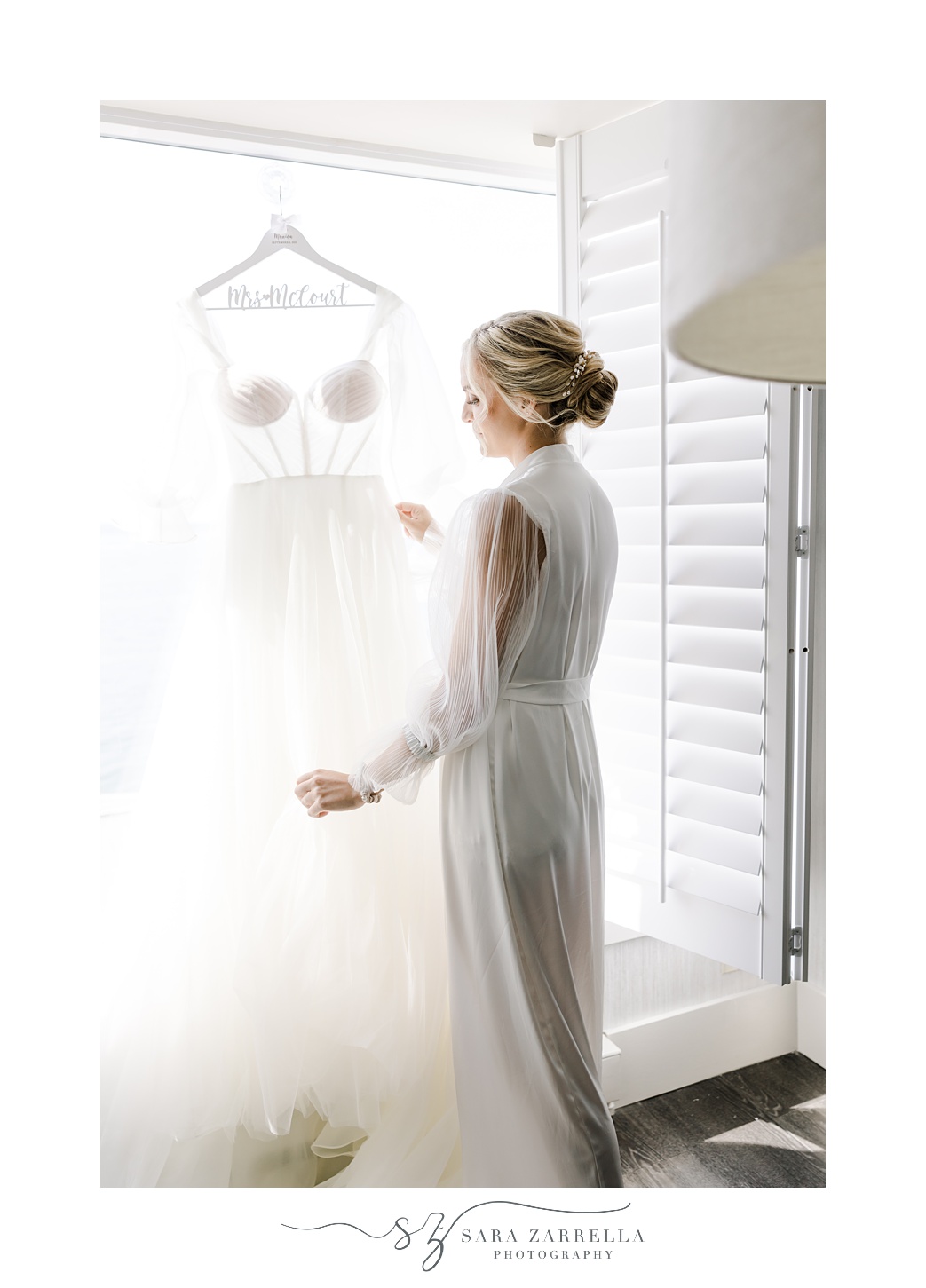 bride stands in window at Newport Harbor Island Resort looking at wedding gown 