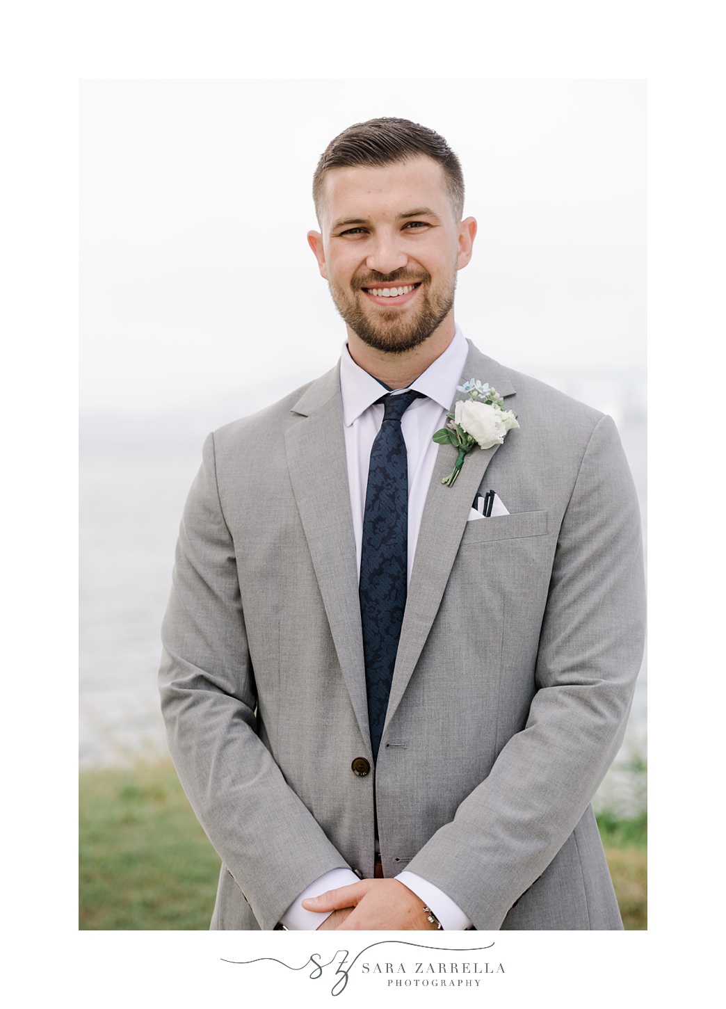 groom stands in grey suit with navy tie outside Newport Harbor Island Resort